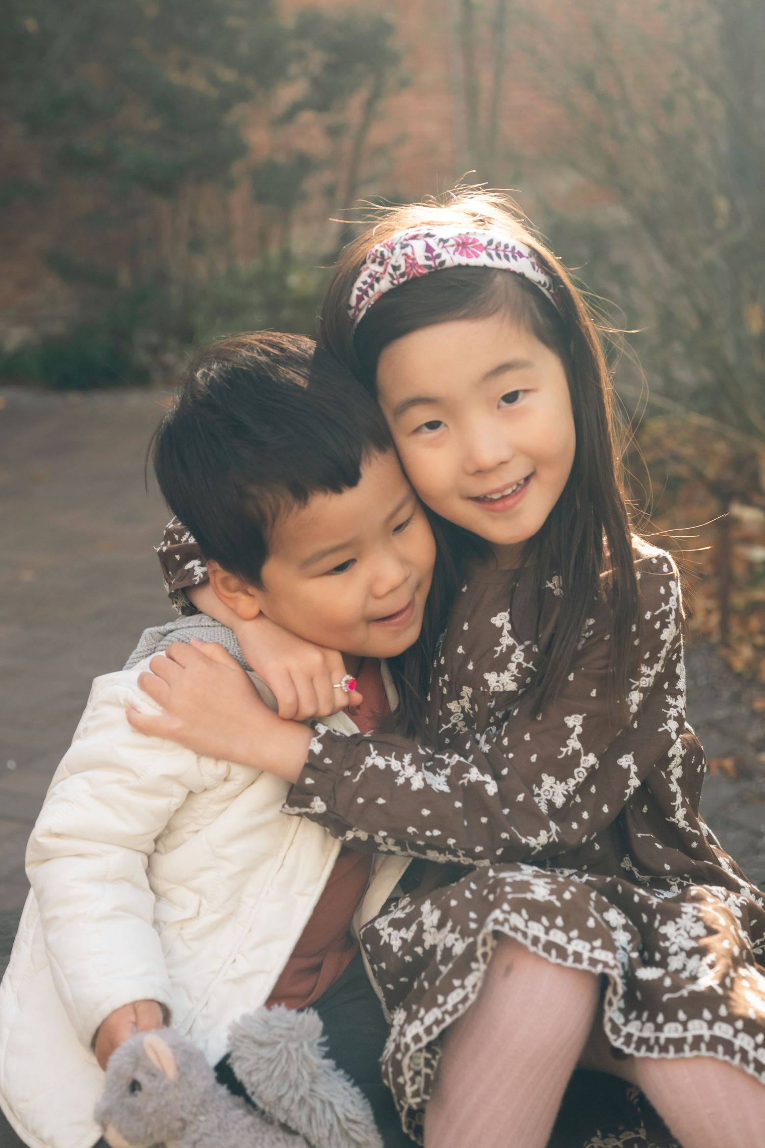 Two children share a sweet candid moment together outdoors while wearing winter coats.