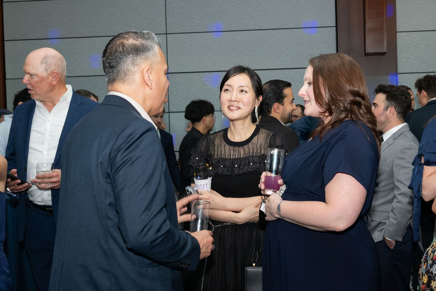 Professionals networking at a formal corporate event, holding drinks and engaging in conversation in a modern venue.