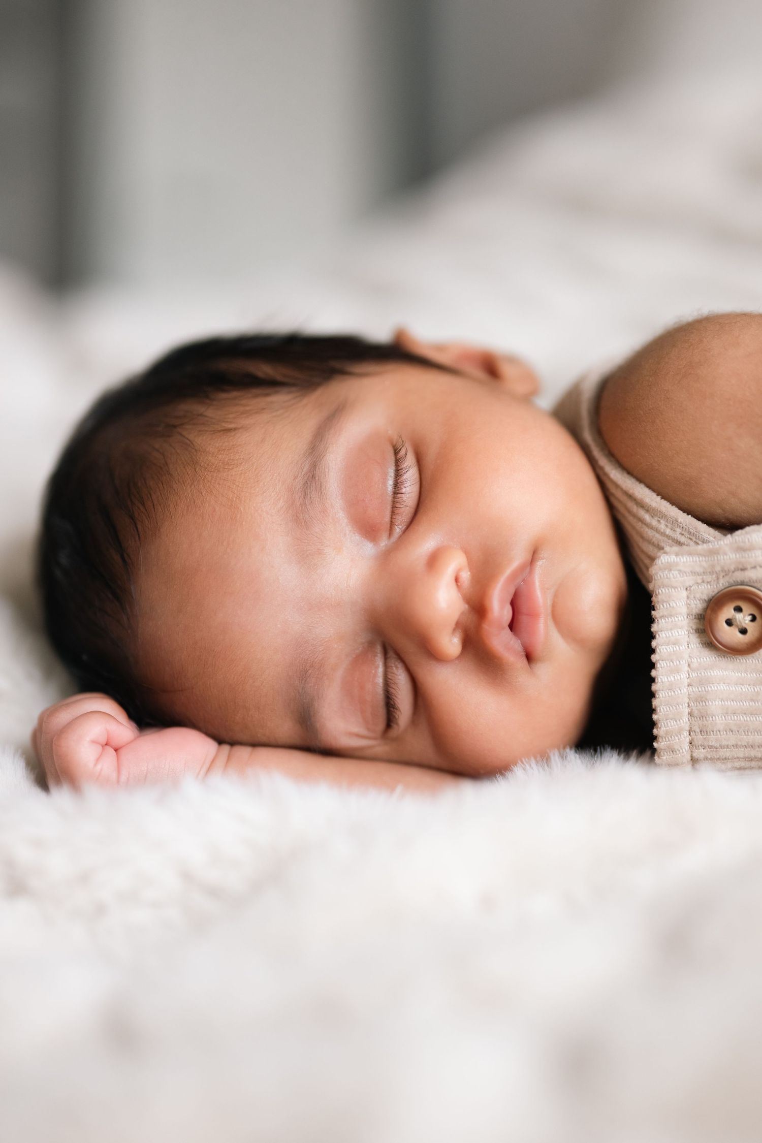 Close-up of a peaceful sleeping newborn baby with soft skin and dark hair resting on white bedding.