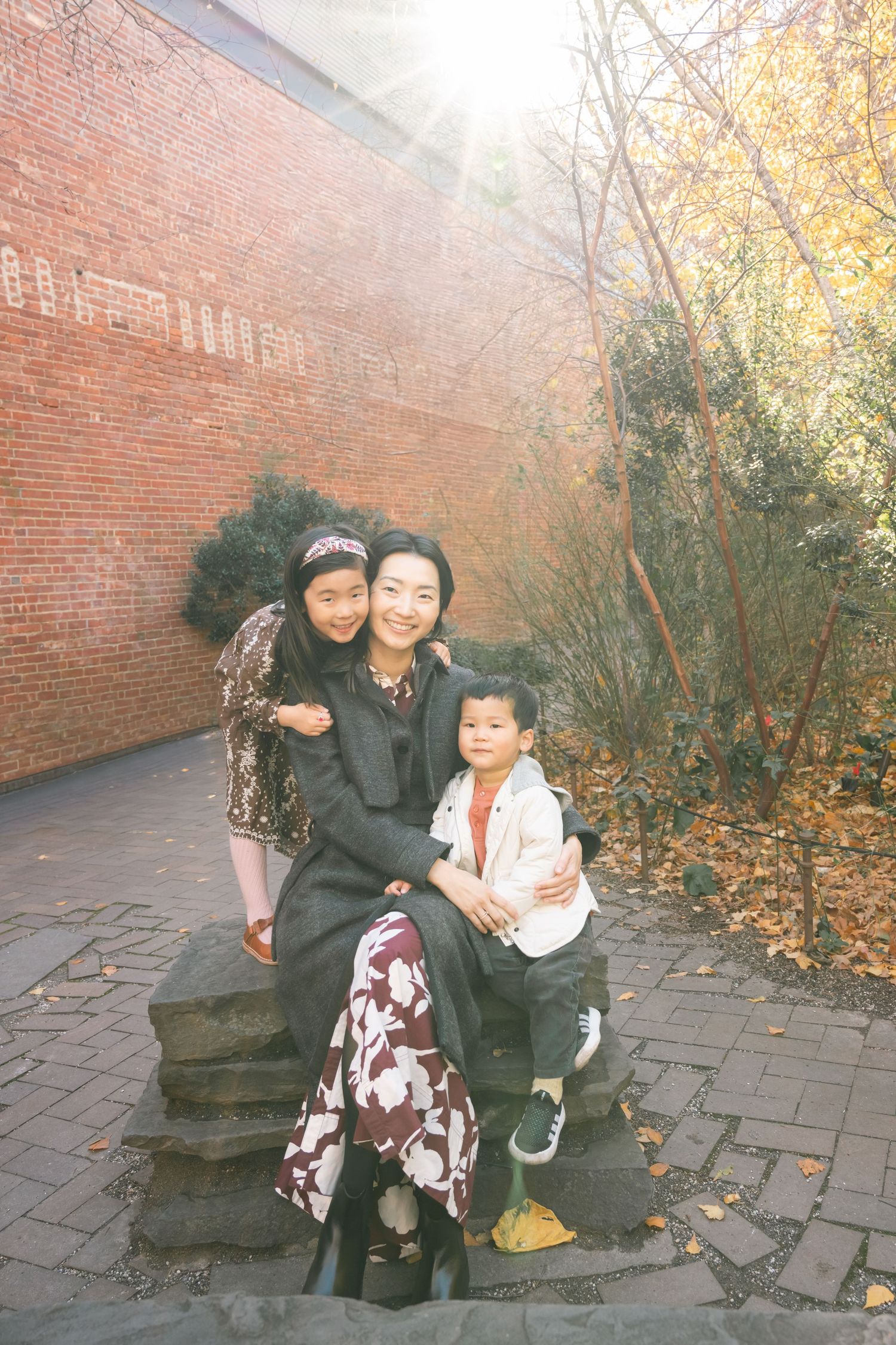 A group sits together on stone steps against a brick wall on an autumn day with fallen leaves scattered nearby.
