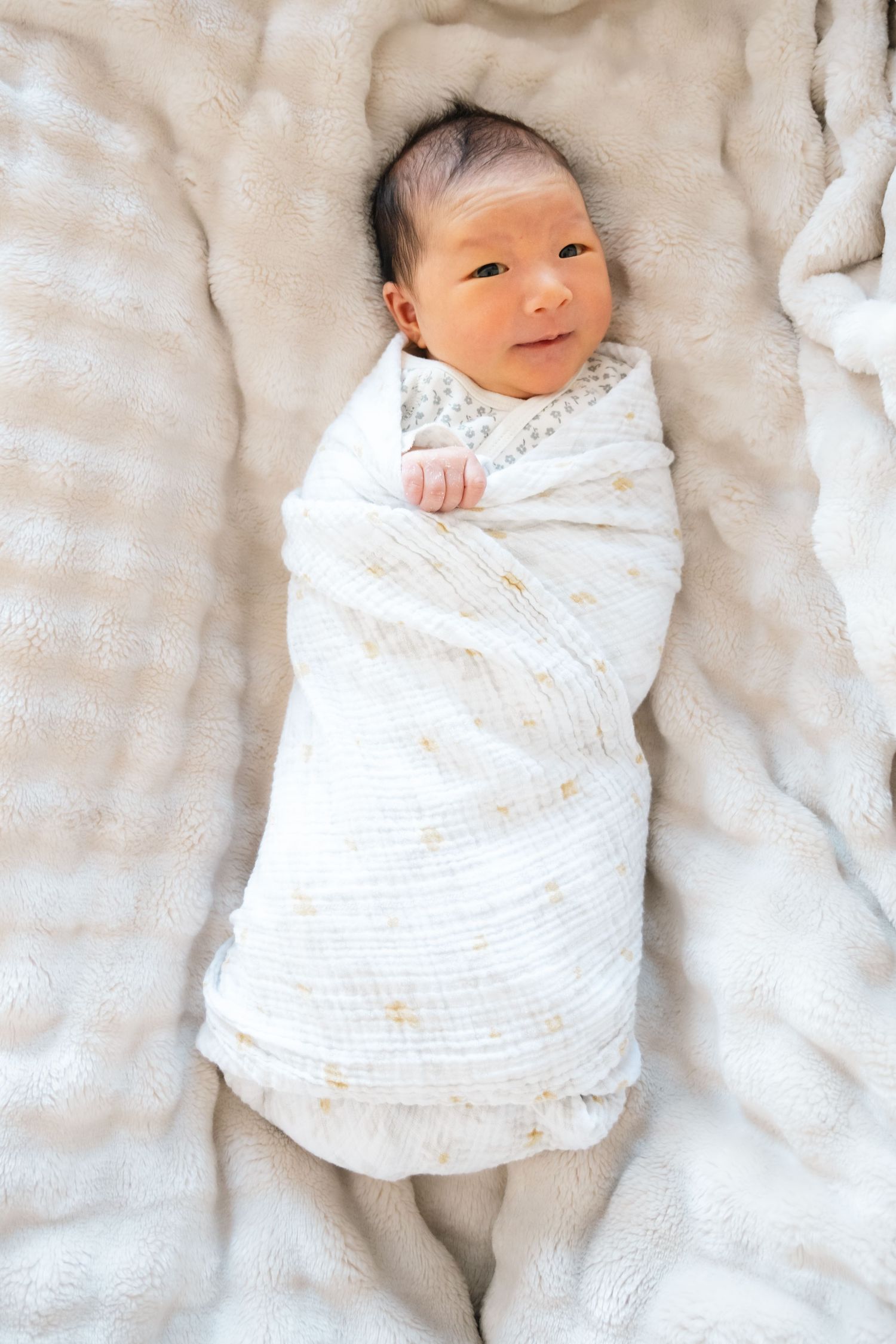 Newborn baby swaddled in white blanket on textured bedding.