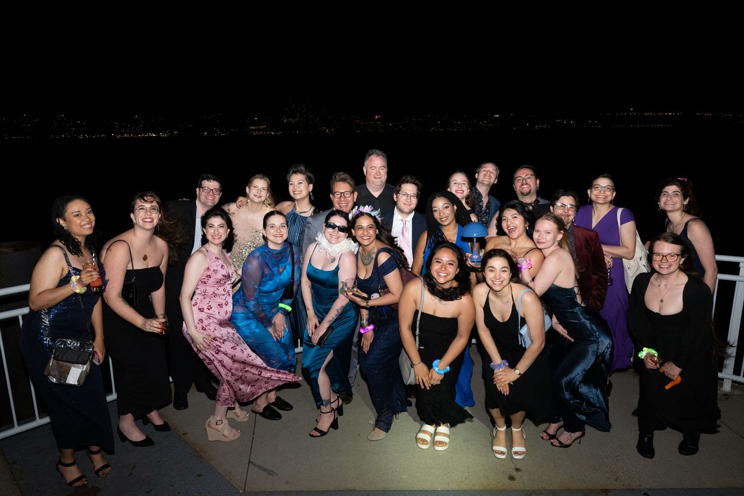 Large group poses together on an outdoor terrace at night with city views.