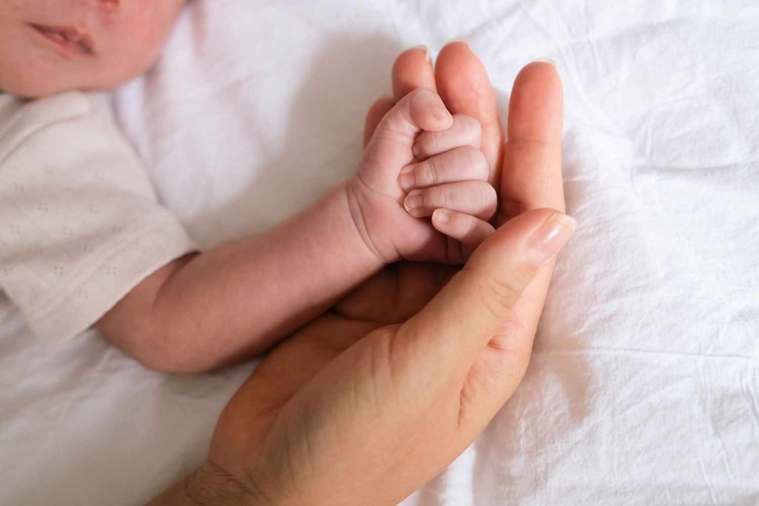 Close-up details of gentle hand holding and tender touches on white sheets.