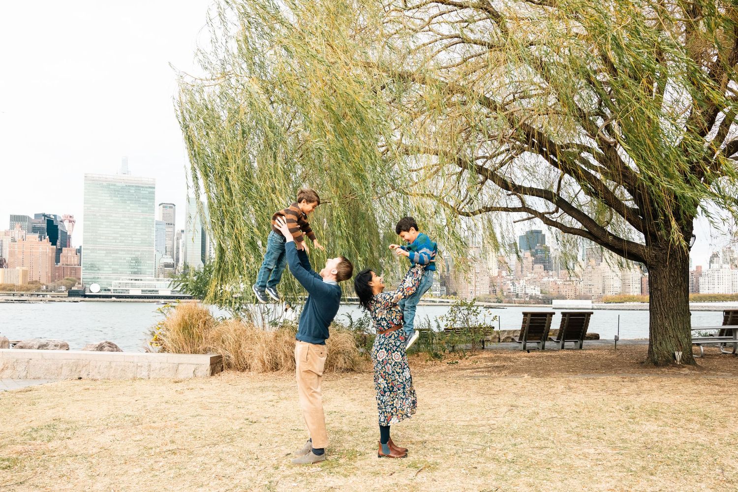 Joyful scene of people jumping and playing in a park with willow trees and city skyline.