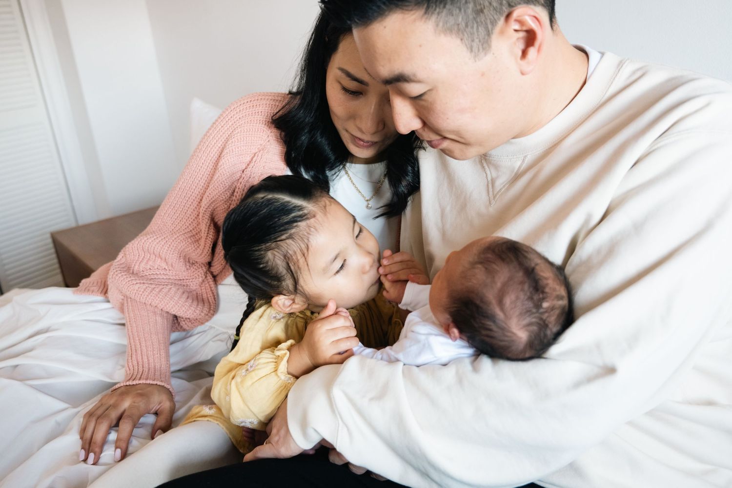 Tender family moments shared on a cozy white bed with a small infant.