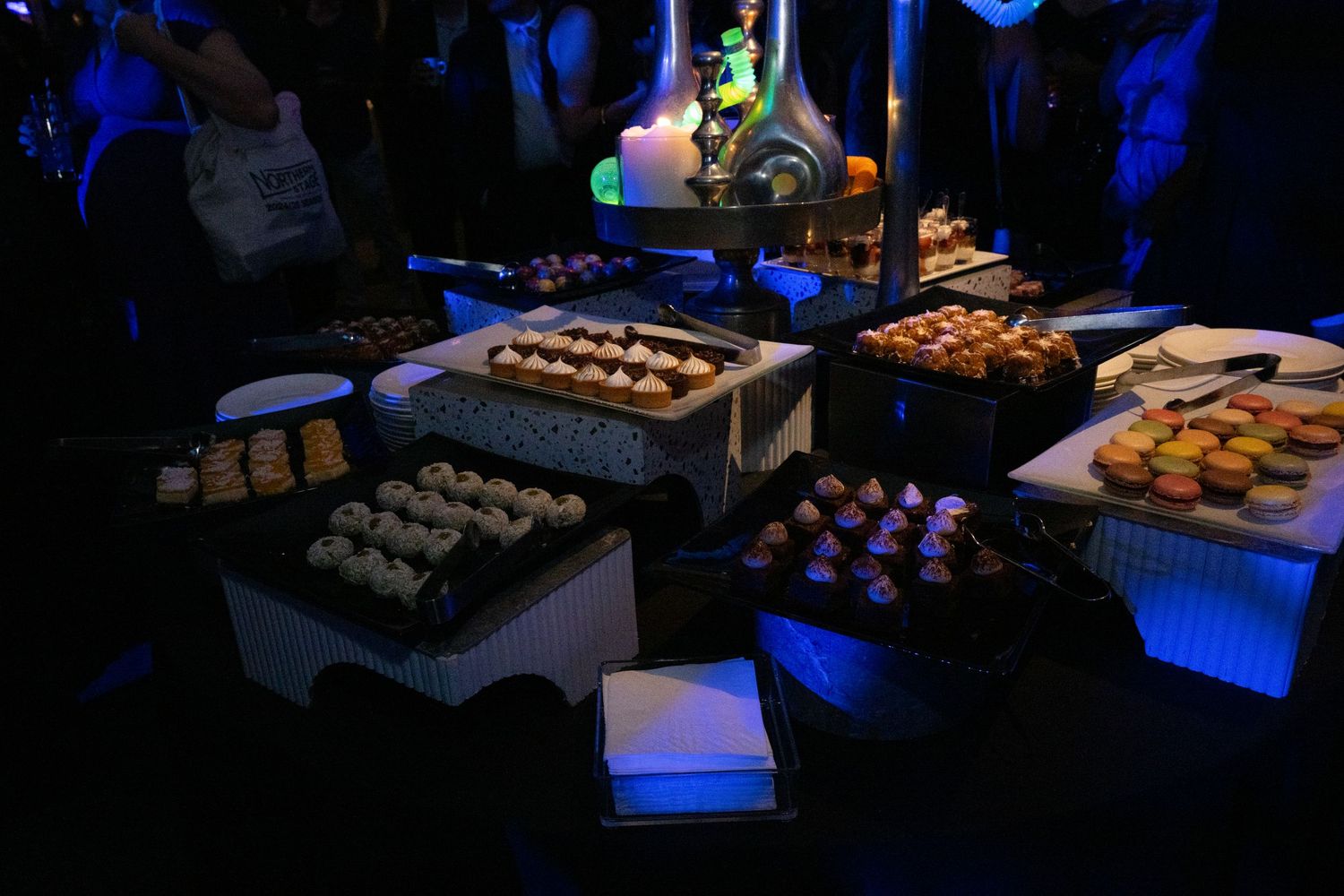 Elegant dessert table display with assorted pastries and treats illuminated by blue event lighting.