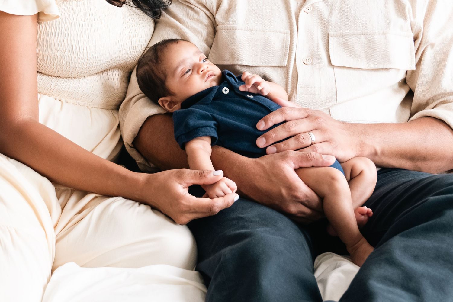 Intimate lifestyle photos of parent cradling newborn baby in casual home setting.