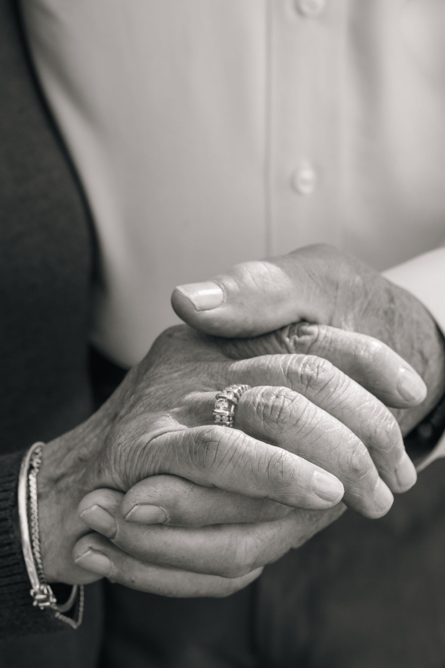 Close-up black and white photo of elderly couple's hands clasped together showing wedding rings.