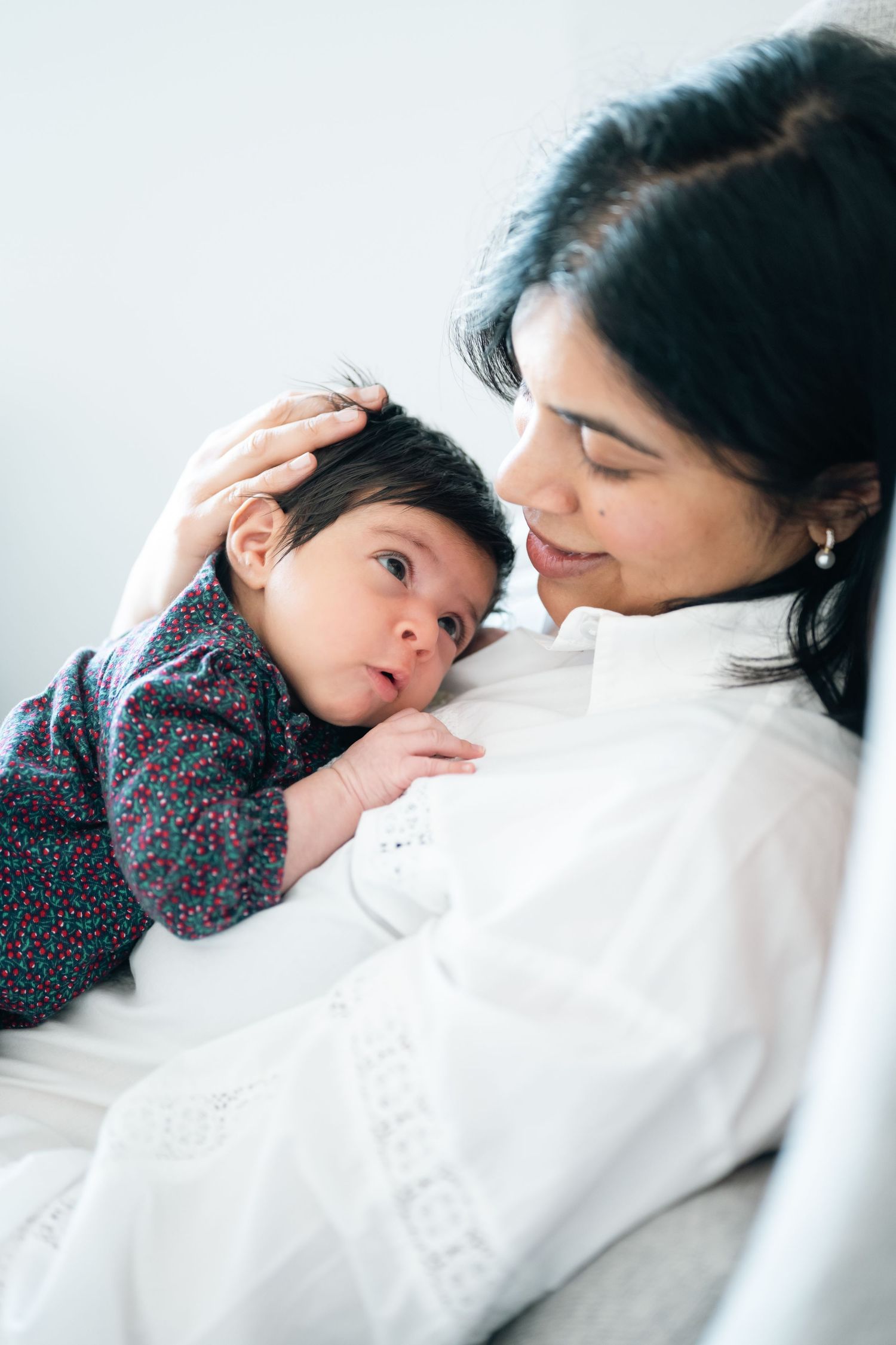A mother tenderly cradles her newborn baby on her chest, gently stroking the infant's dark hair.