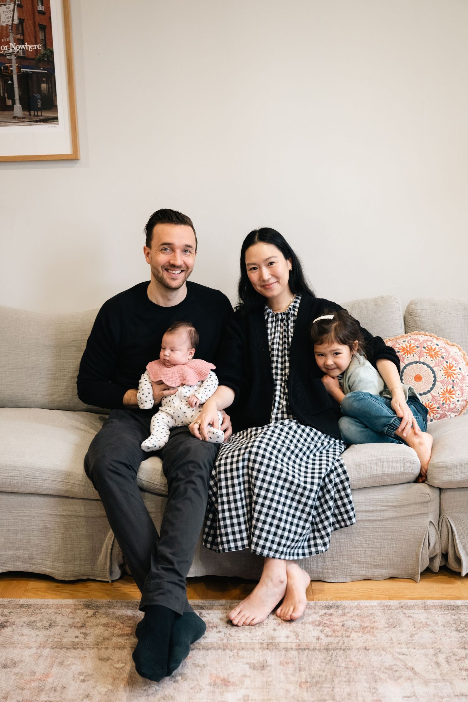 A family relaxes together on a grey couch in a cozy living room with decorative pillows and minimal decor.