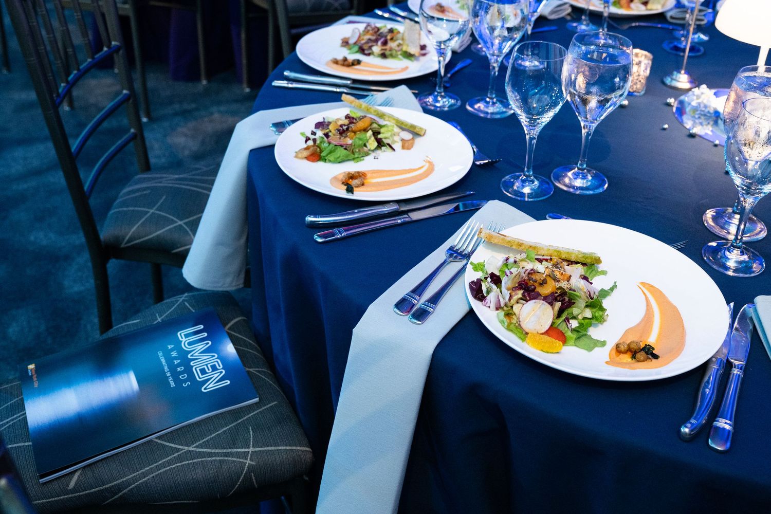Elegant navy blue table setting with plated salads and crystal glassware at a formal dinner.