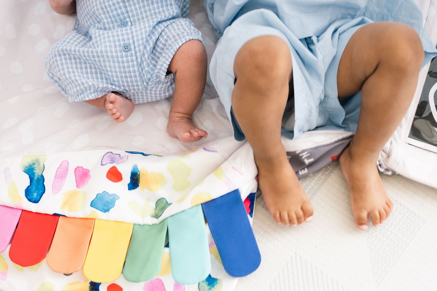 Children's feet next to colorful rainbow artwork on white surface.