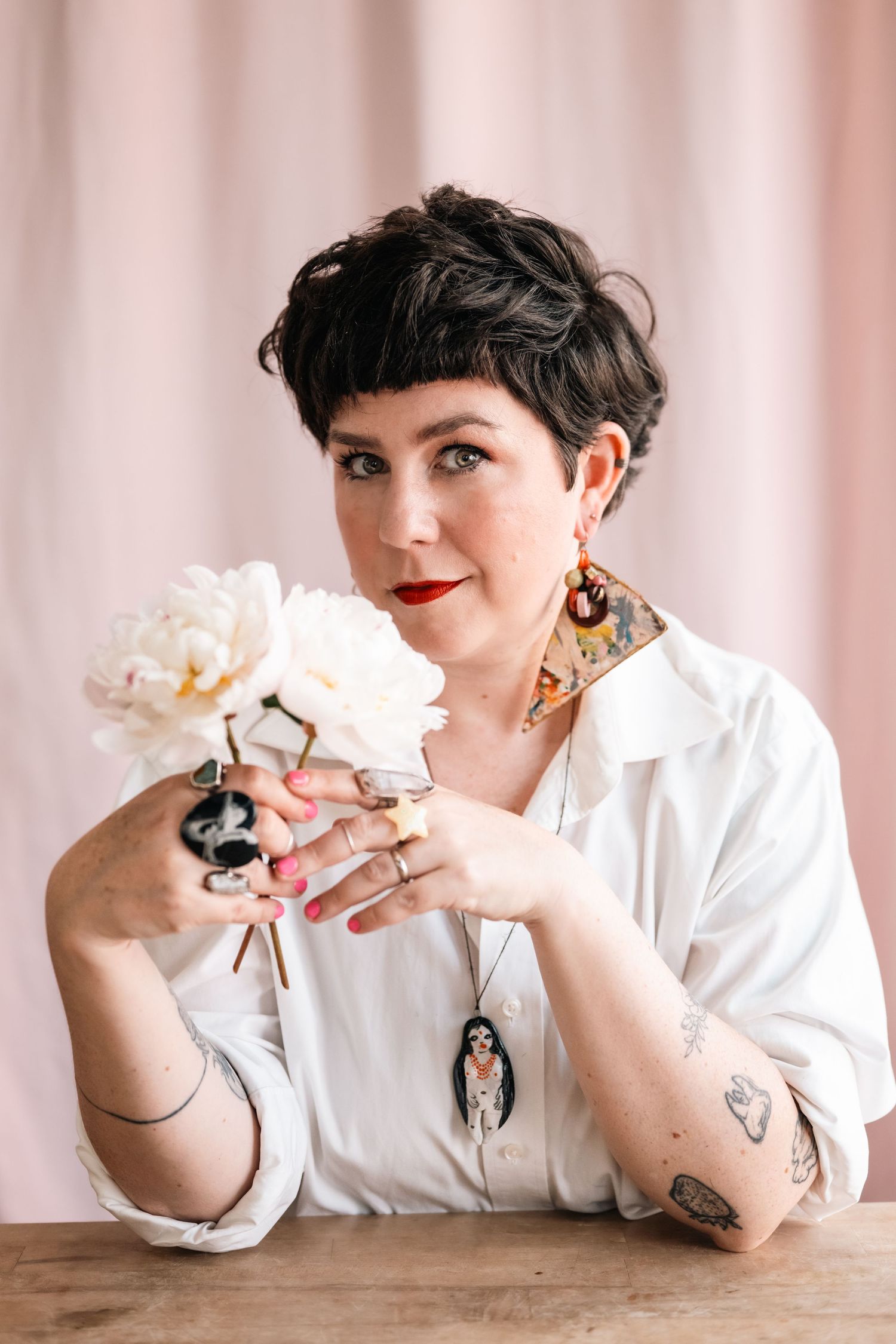 Person in white shirt plays with white flowers against pink backdrop in creative portrait series.