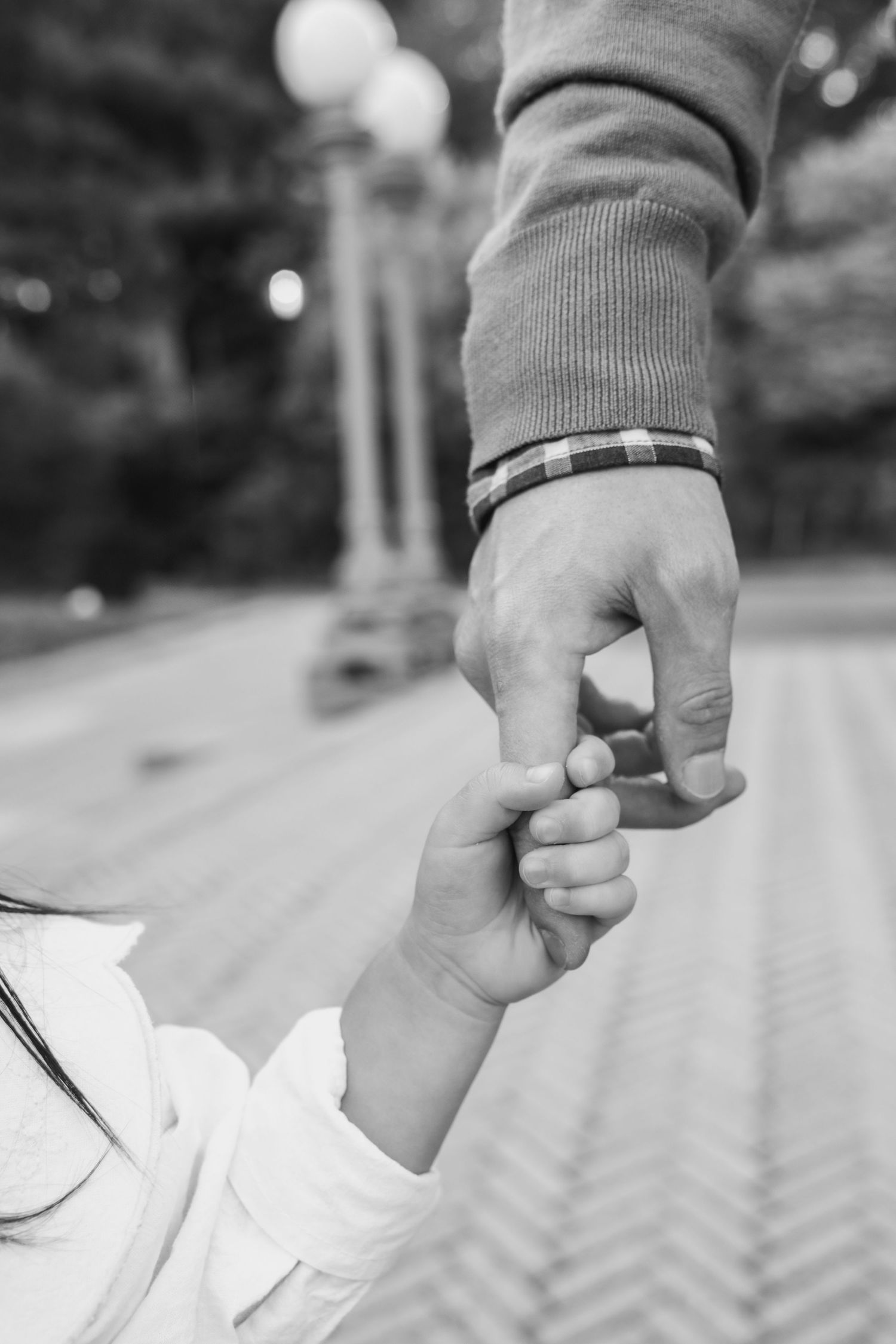 Black and white close-up of adult and child holding hands outdoors.