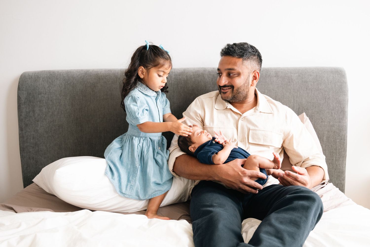 Parents share tender moments with their newborn baby while relaxing on a gray couch.