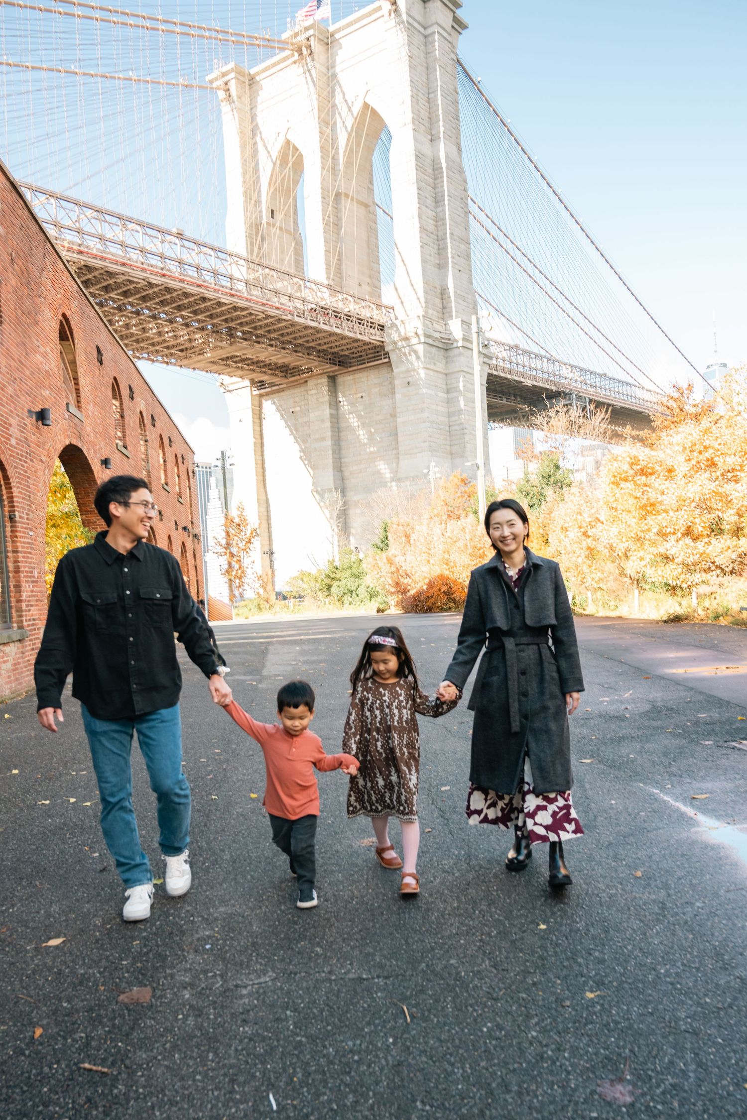 A family takes a stroll together under the iconic Brooklyn Bridge on an autumn day in New York City.