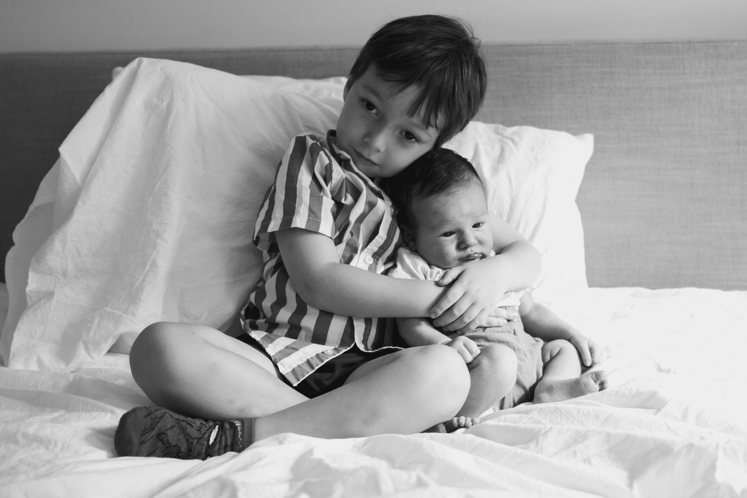 Family members resting together on white bedding in natural light.