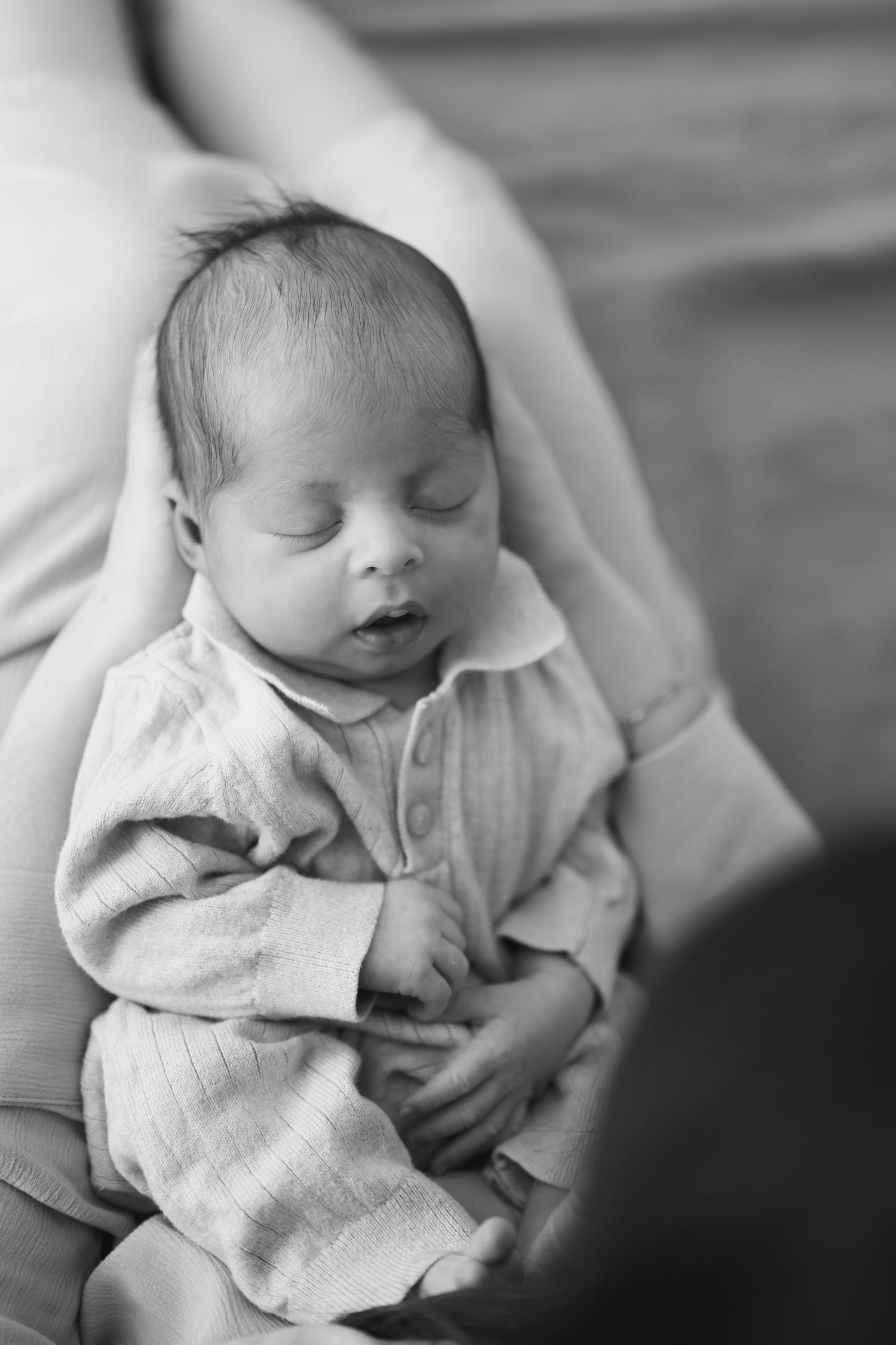 Black and white close-up photos of newborn baby being cradled in soft lighting.