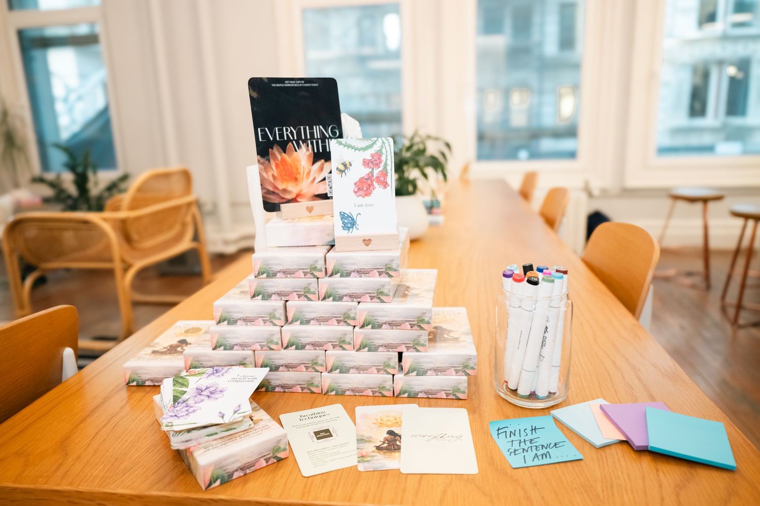 A wooden table displays stacked wrapped gifts, markers, cards, and a book titled Everything in a bright room.