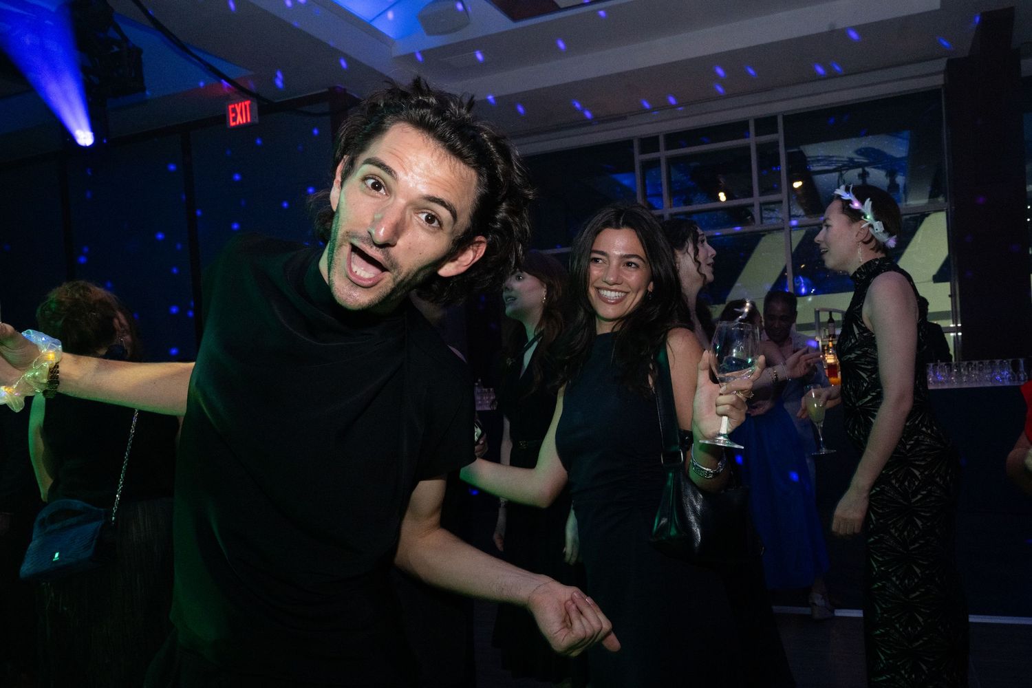 People dancing and celebrating at a lively nightclub party with blue ambient lighting.