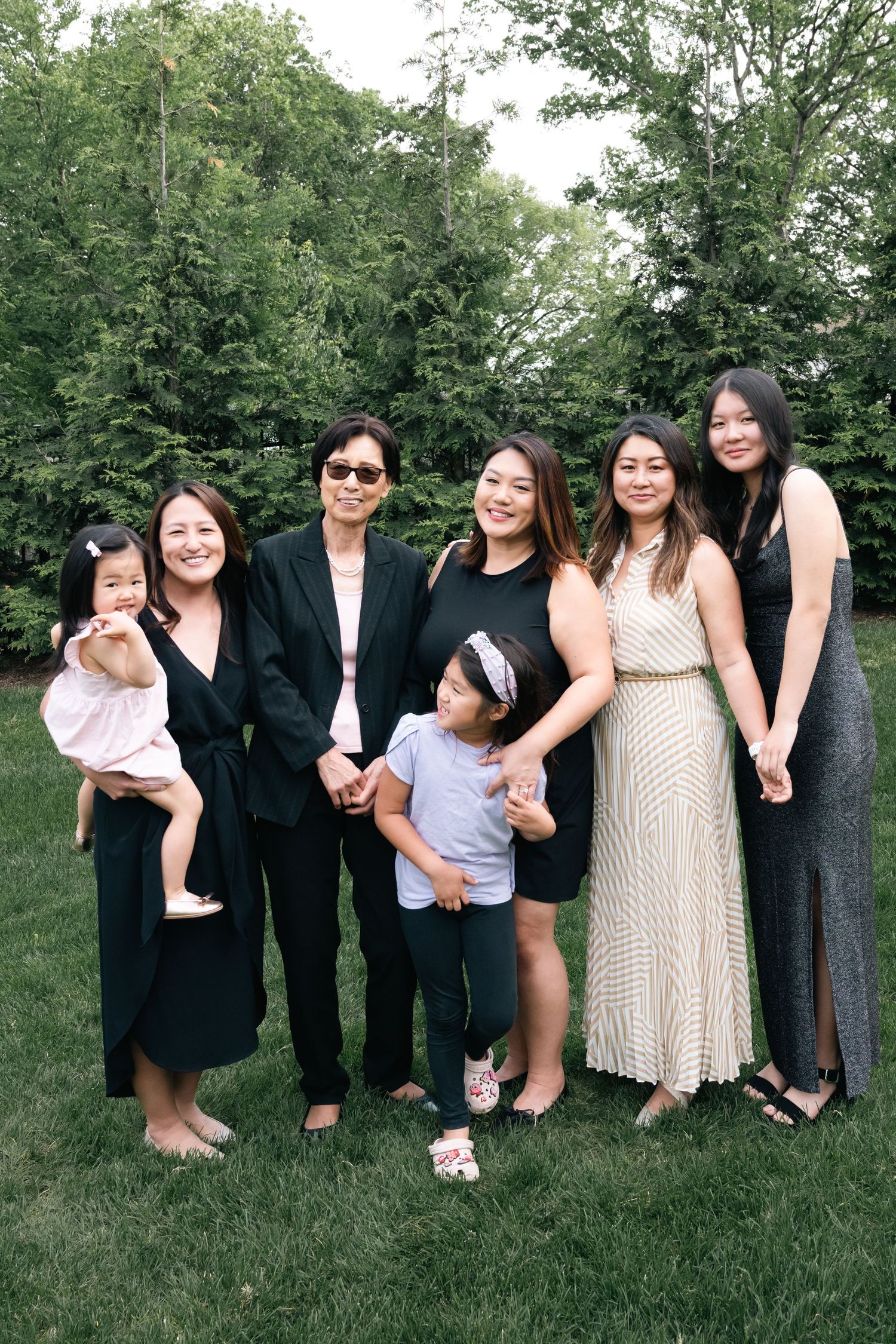 A large family group poses together on grass wearing a mix of formal and casual attire.