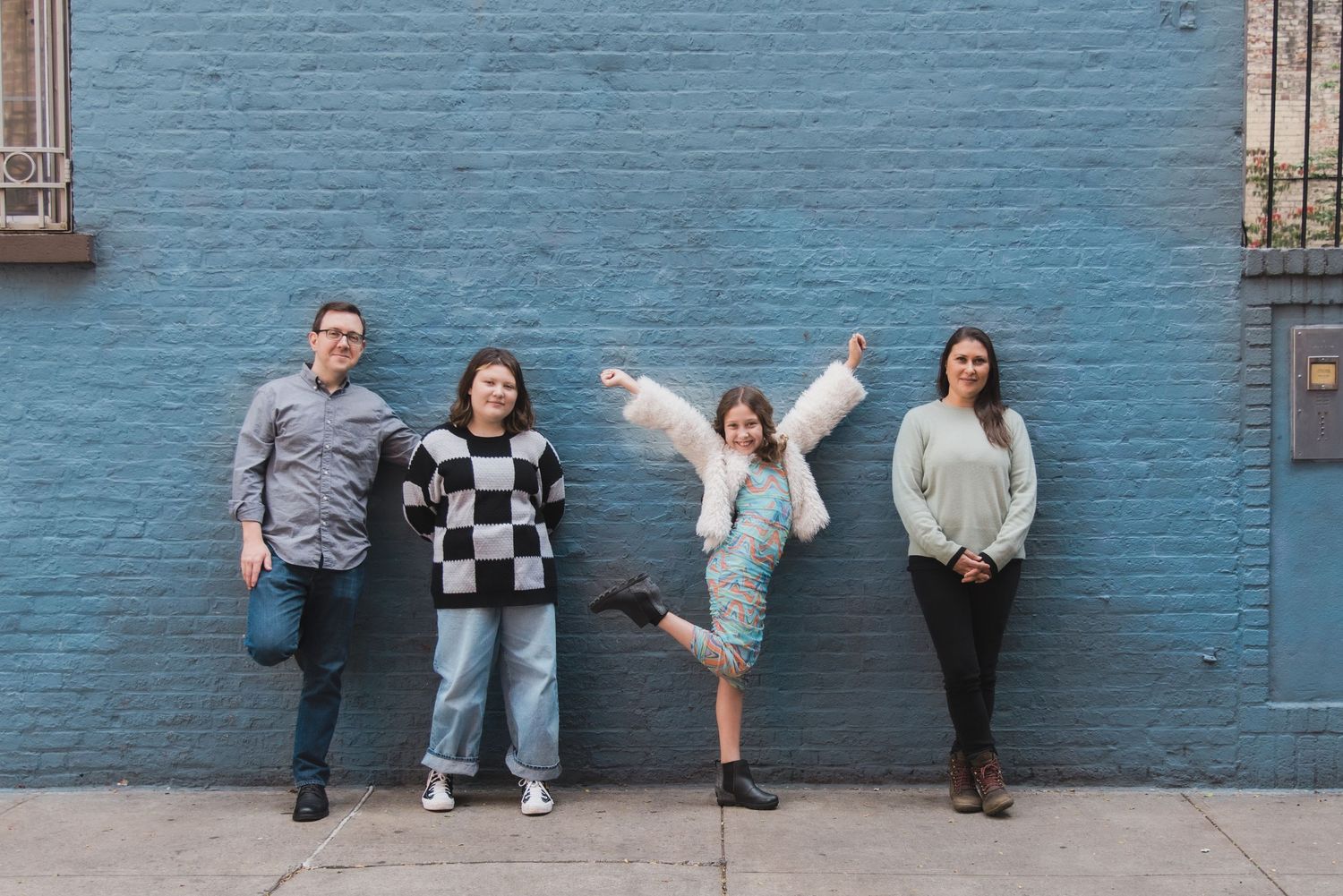 Group making fun poses against a vibrant blue wall outdoors.