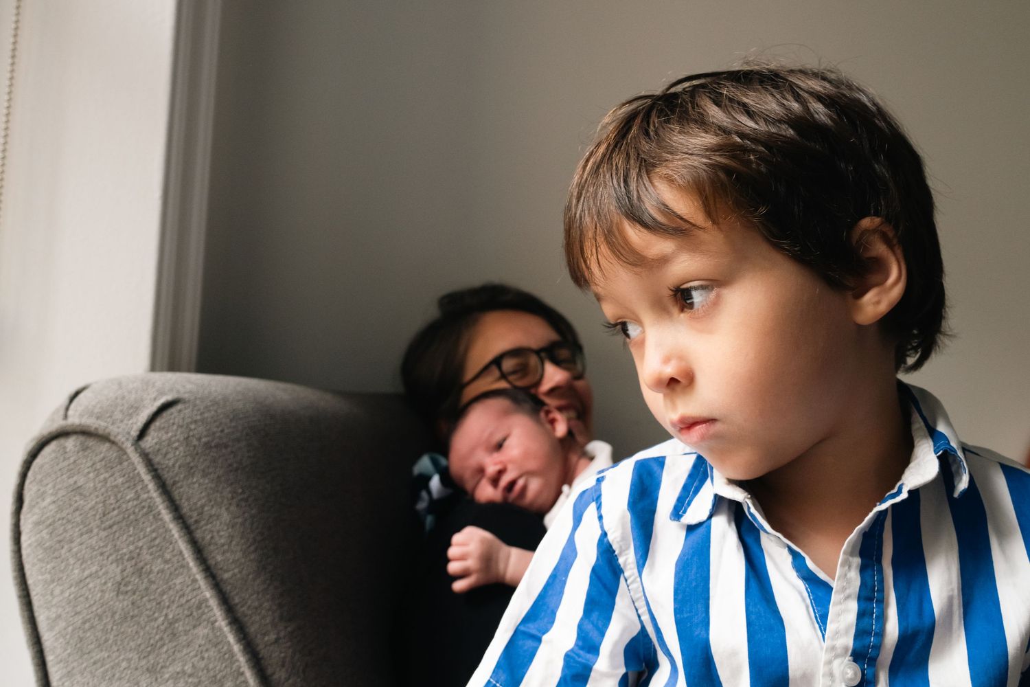 Child in blue striped shirt resting on gray couch near window.