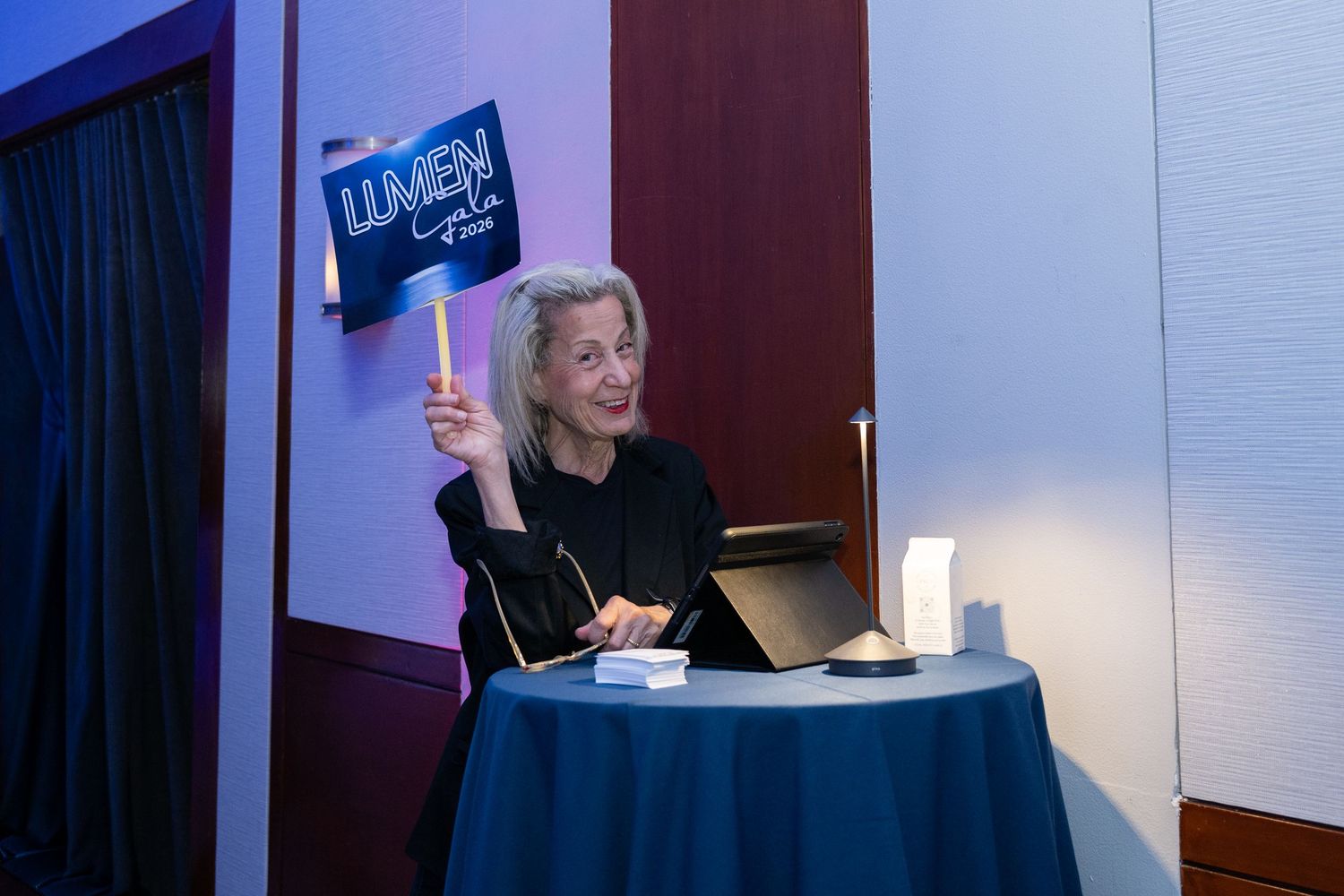 Woman holding a Lumen sign at a registration desk during a corporate event.