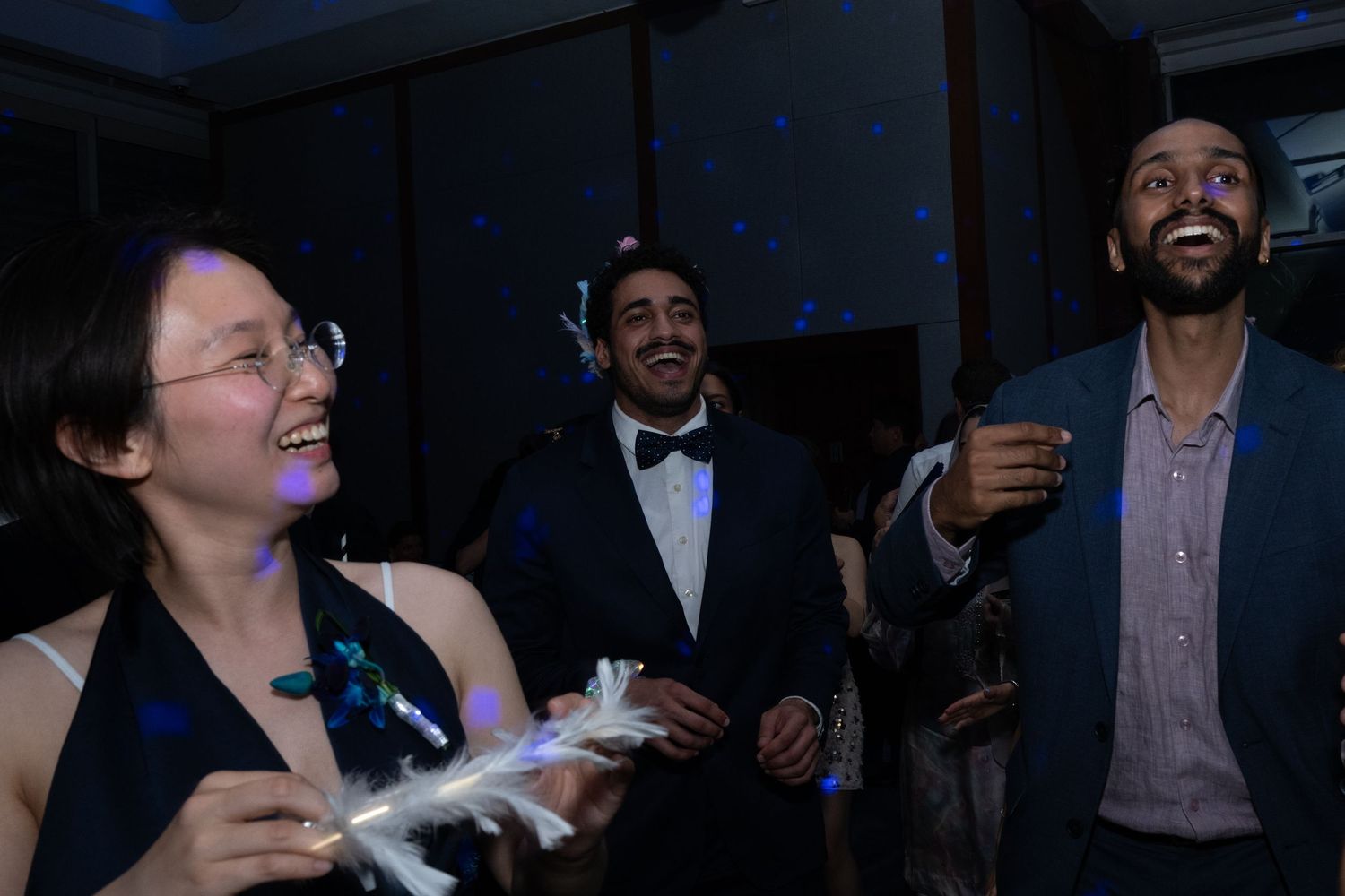 Three people laughing and dancing at a formal event, with blue star-lit backdrop and festive atmosphere.