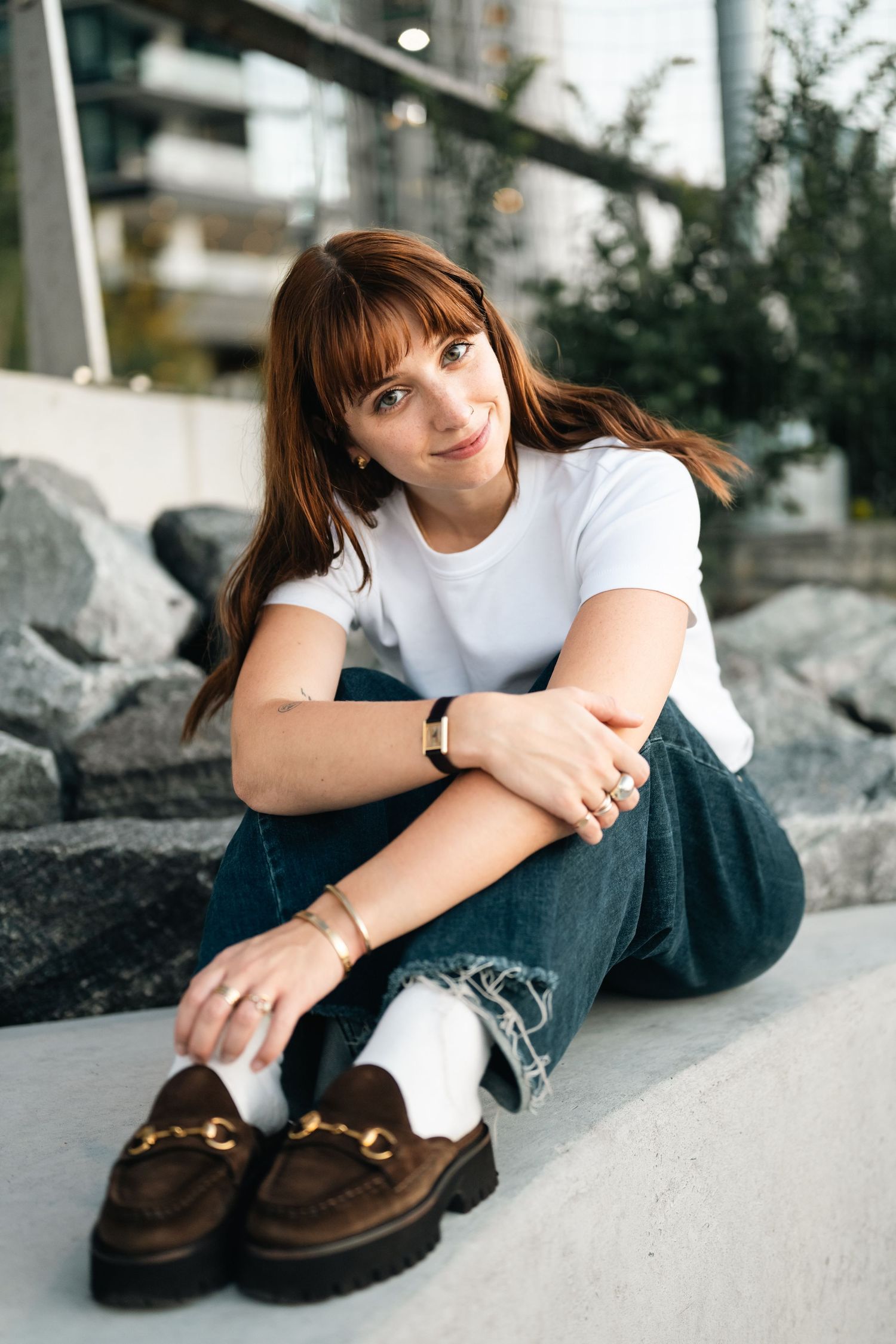 Person in white t-shirt and jeans sitting casually on concrete with brown loafers.