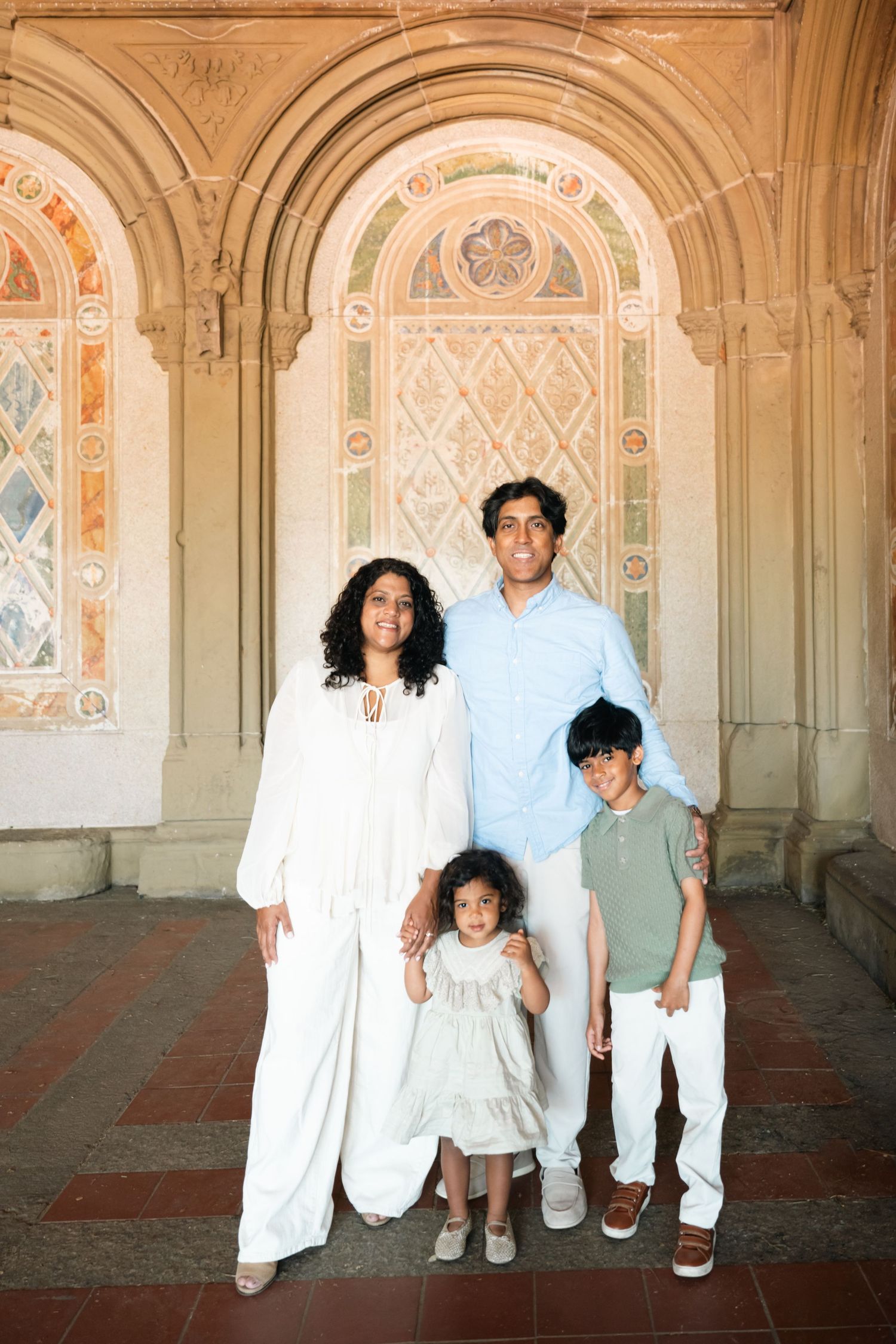 A family of four poses together under ornate arched stonework at Bethesda Terrace in Central Park, NYC.