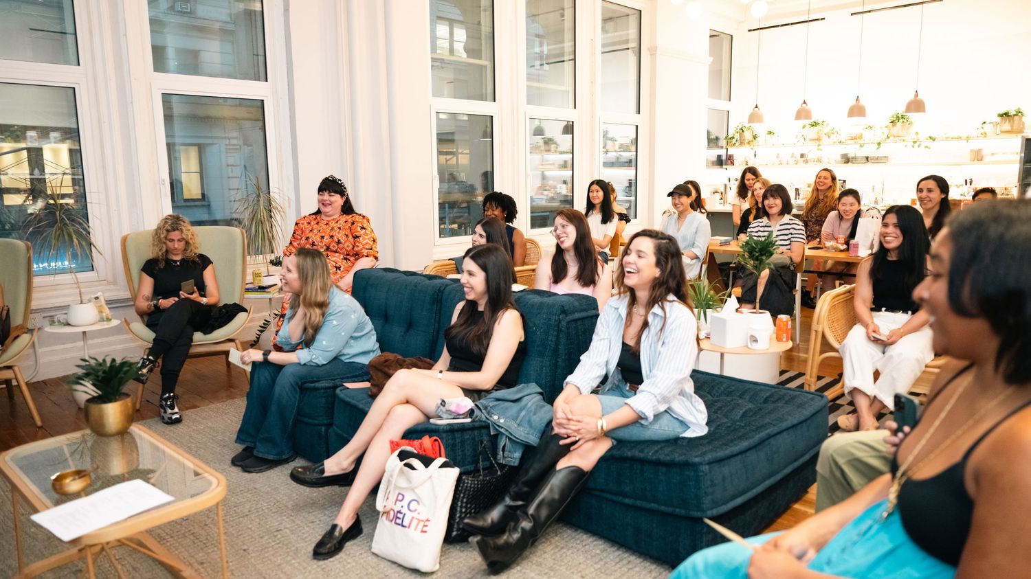 Diverse group of women attending an indoor networking event, seated on couches in a modern bright space.