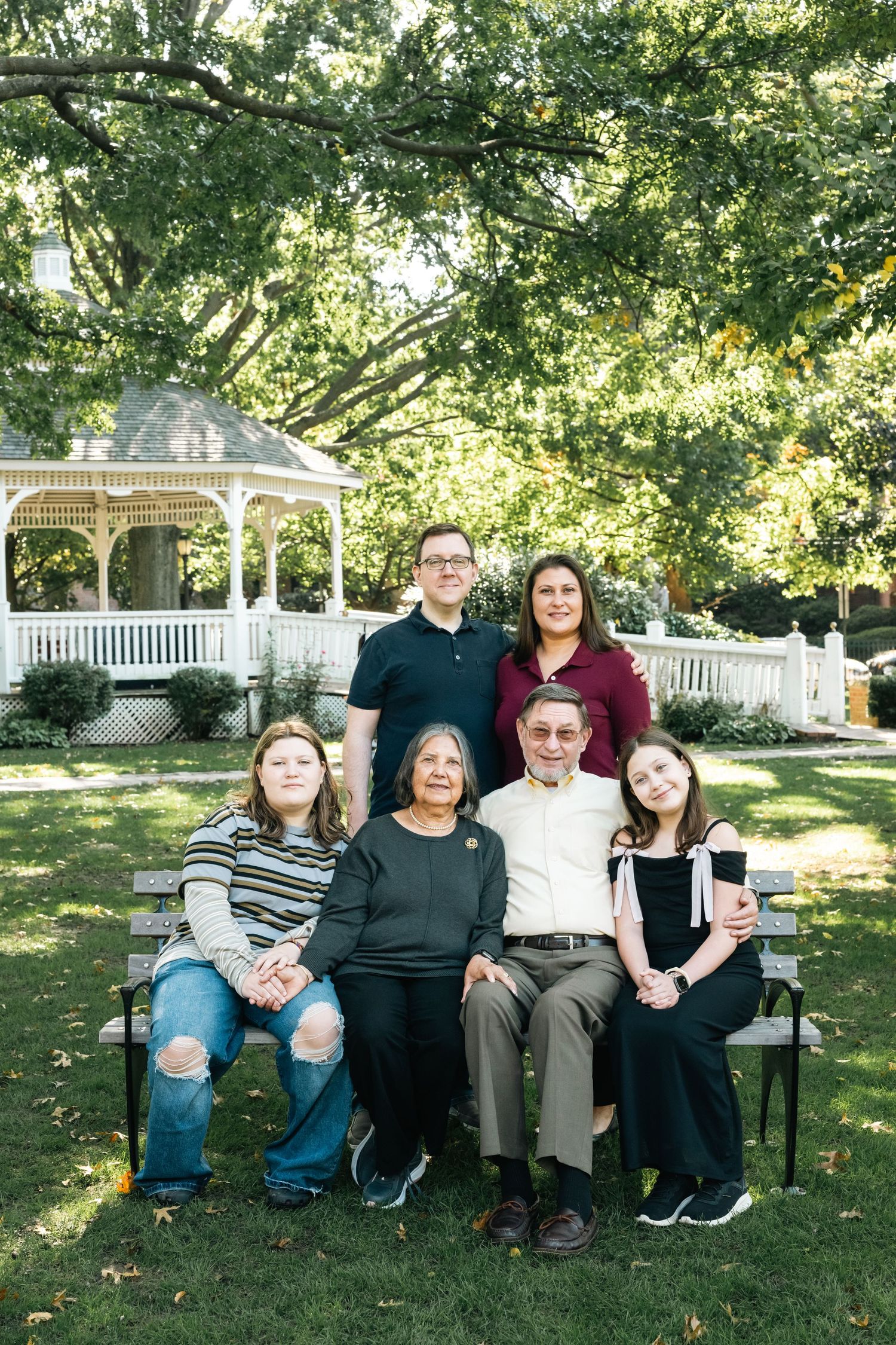 Family sitting together on outdoor benches in a garden setting with a white gazebo in the background.