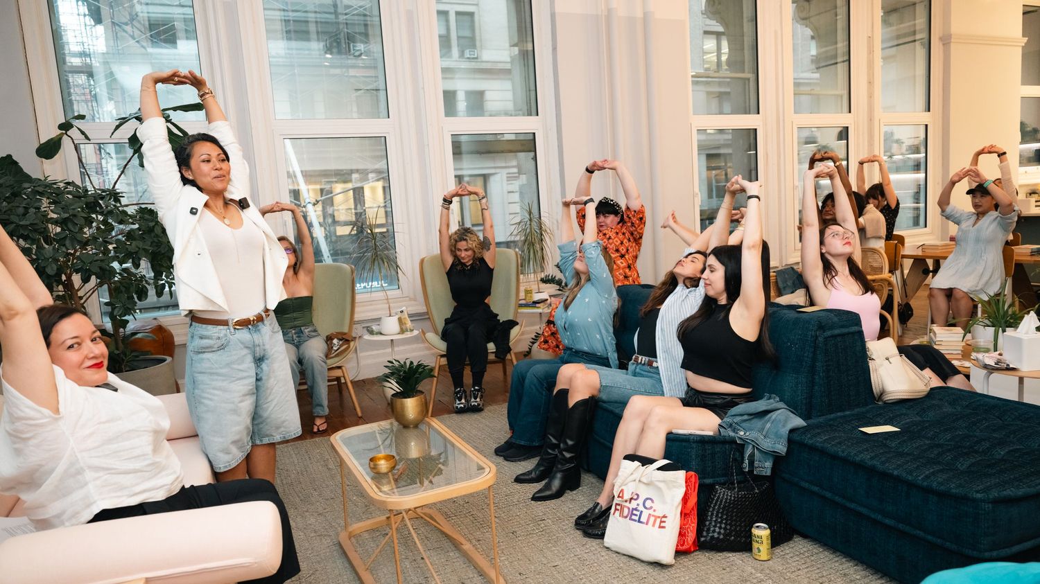 Group of women raising hands and taking selfies during a lively indoor social gathering in a bright modern space.