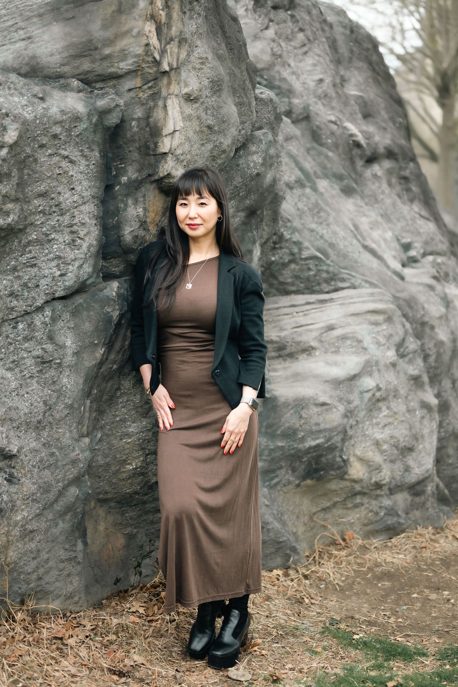 Fashion portrait against textured rock formations with black blazer and brown dress.