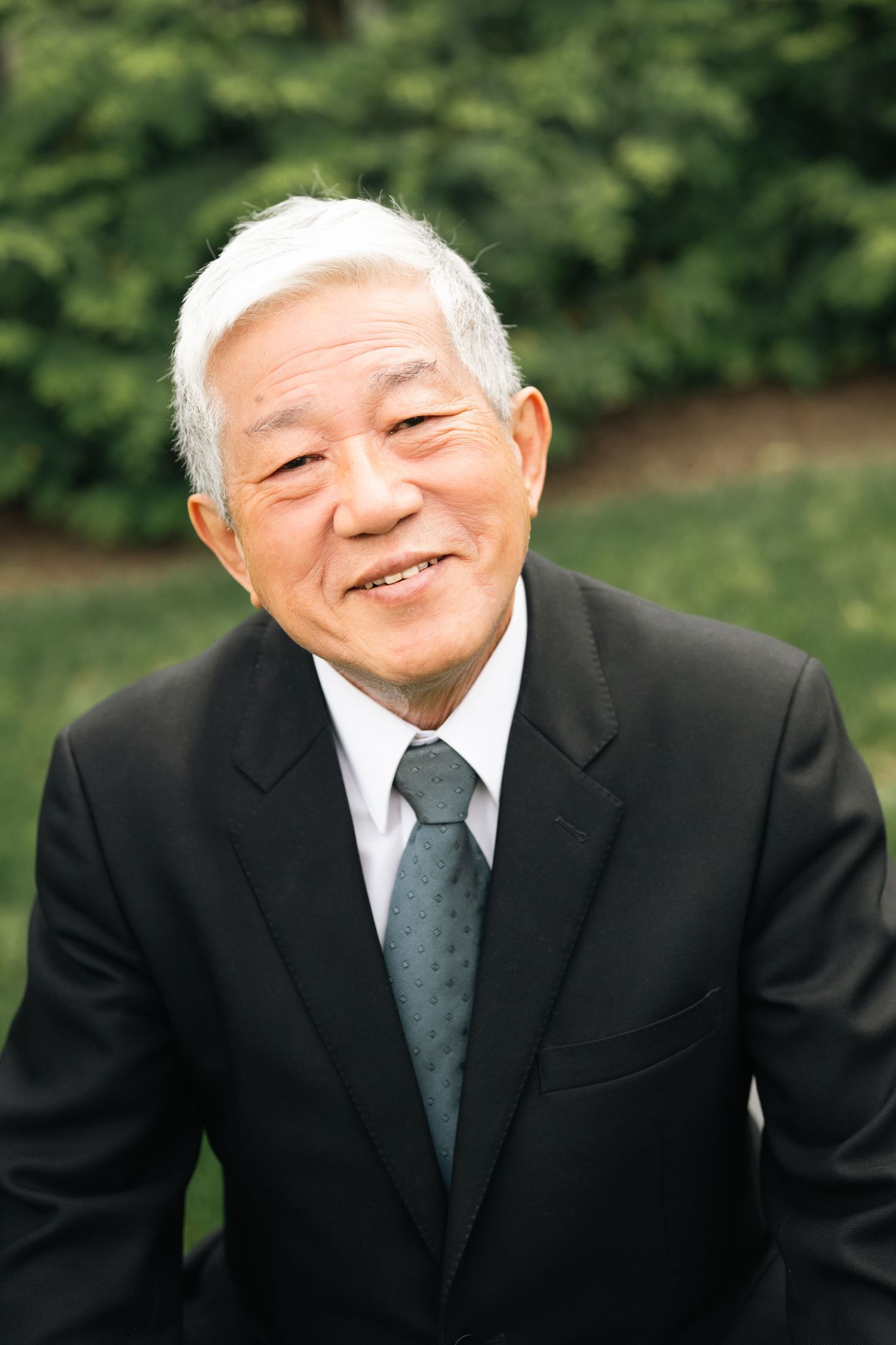 A person in a black suit and tie smiles warmly in a series of outdoor portrait shots.