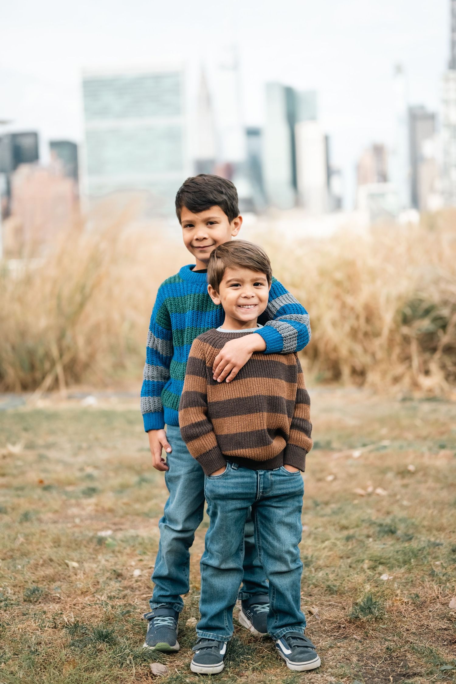 Two children in casual wear playing together outdoors against an urban background.