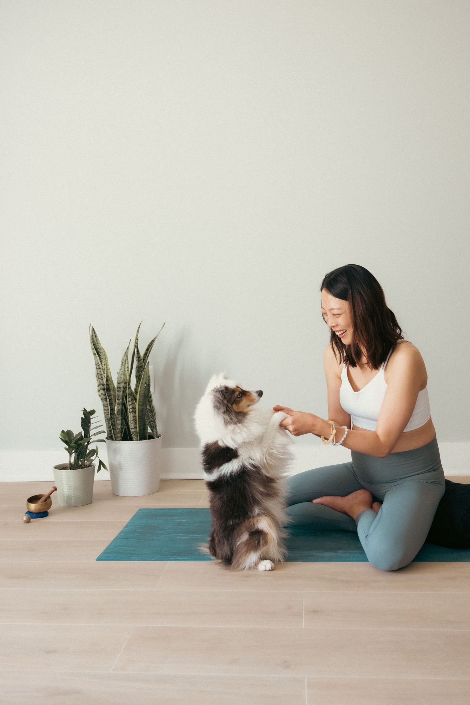 Person playing with a fluffy cat while sitting on a yoga mat in a bright room.