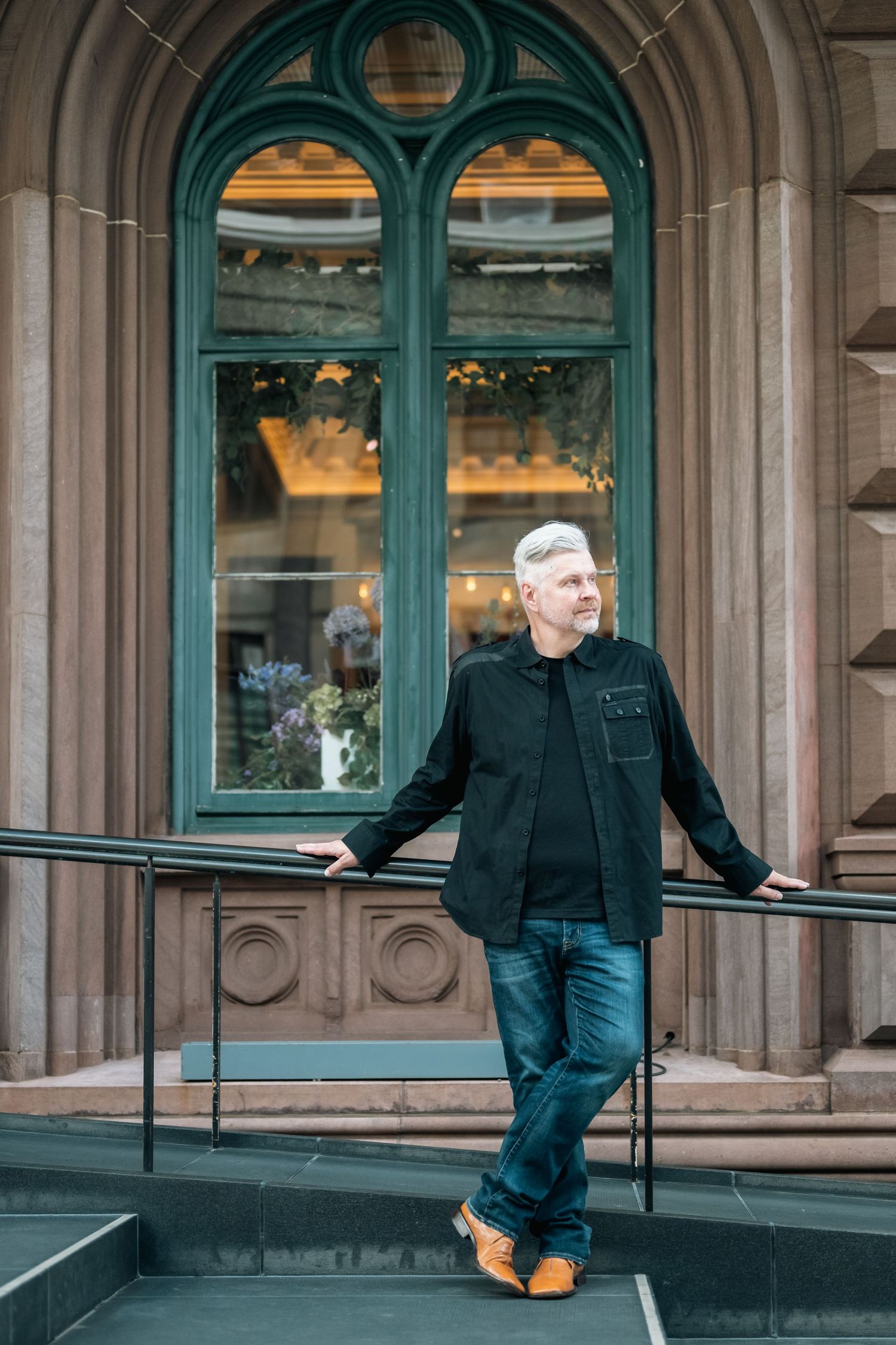 Person in black clothing posing playfully outside historic building with turquoise archways.