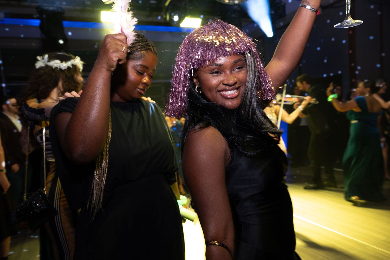 Two women dancing joyfully at a lively evening gala with sparkling decorations.