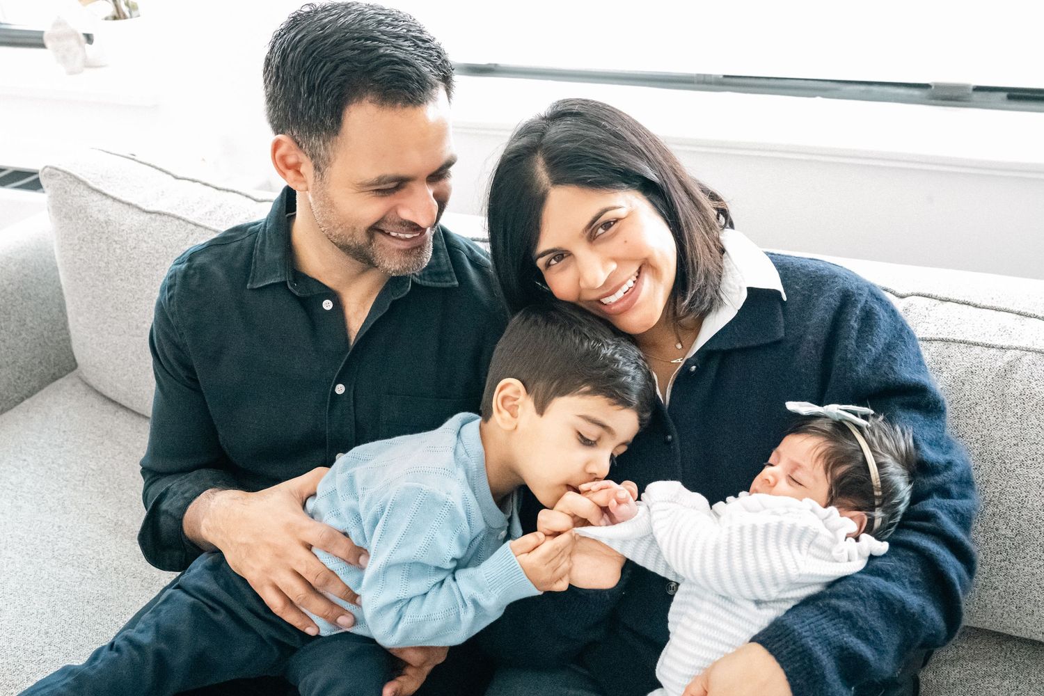 Happy family of four with newborn baby sitting together on a cozy sofa, sharing a warm moment.