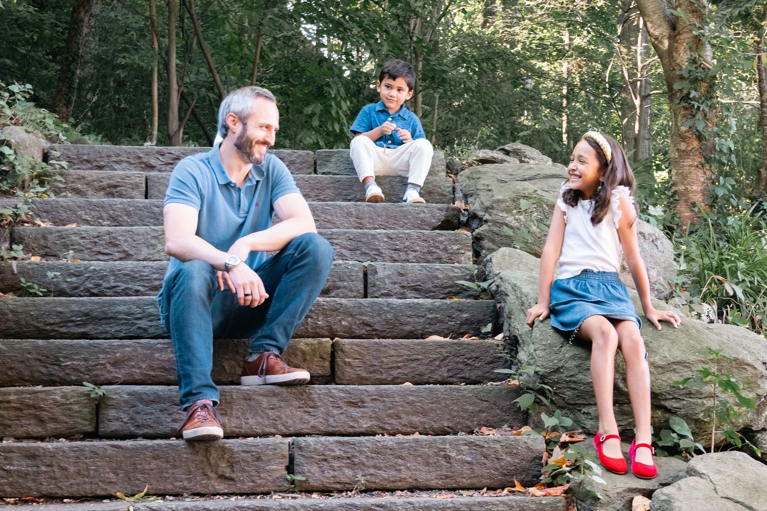 Two people sitting on rustic stone steps having a conversation in a wooded outdoor setting.