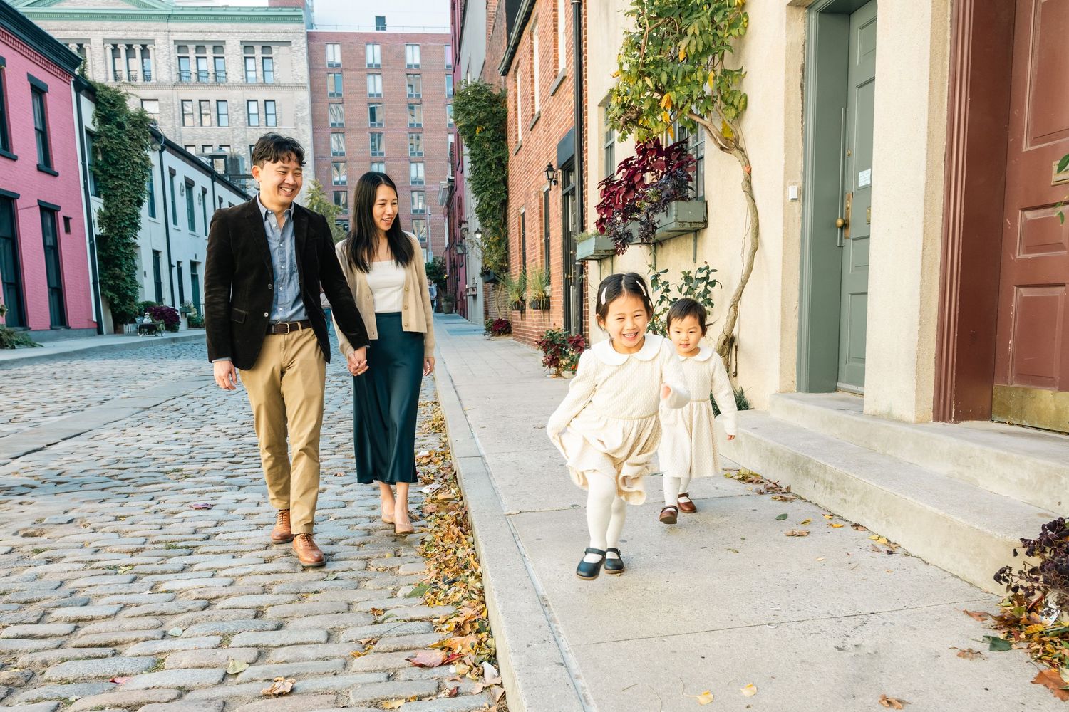 People walking along a historic cobblestone street lined with buildings in an urban neighborhood.