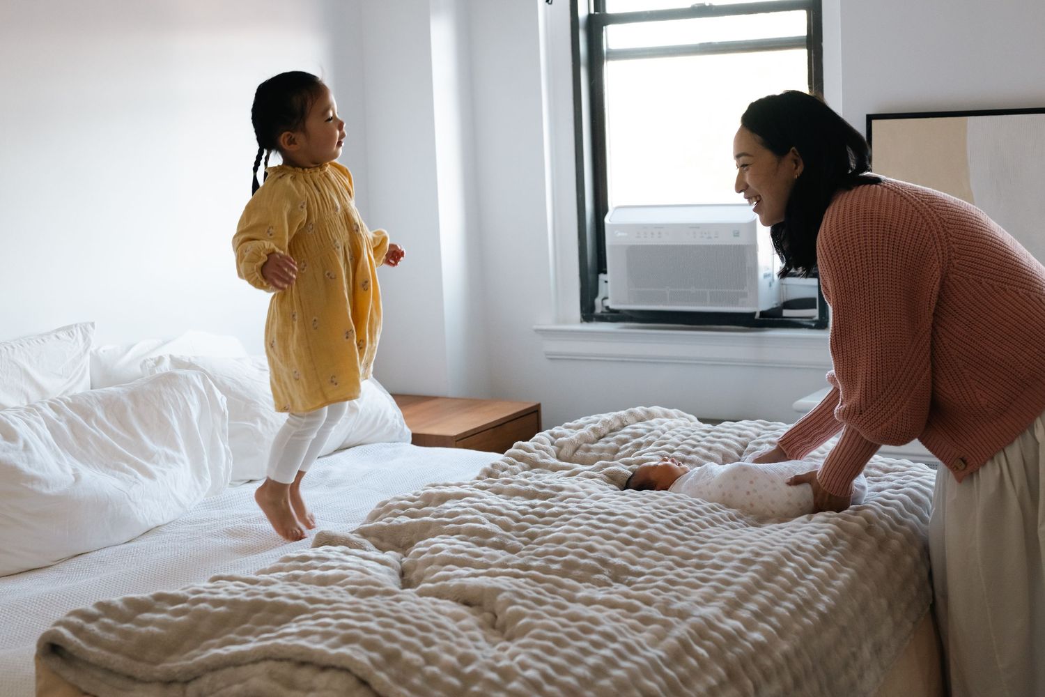 Family members interacting playfully on a bright white bed.