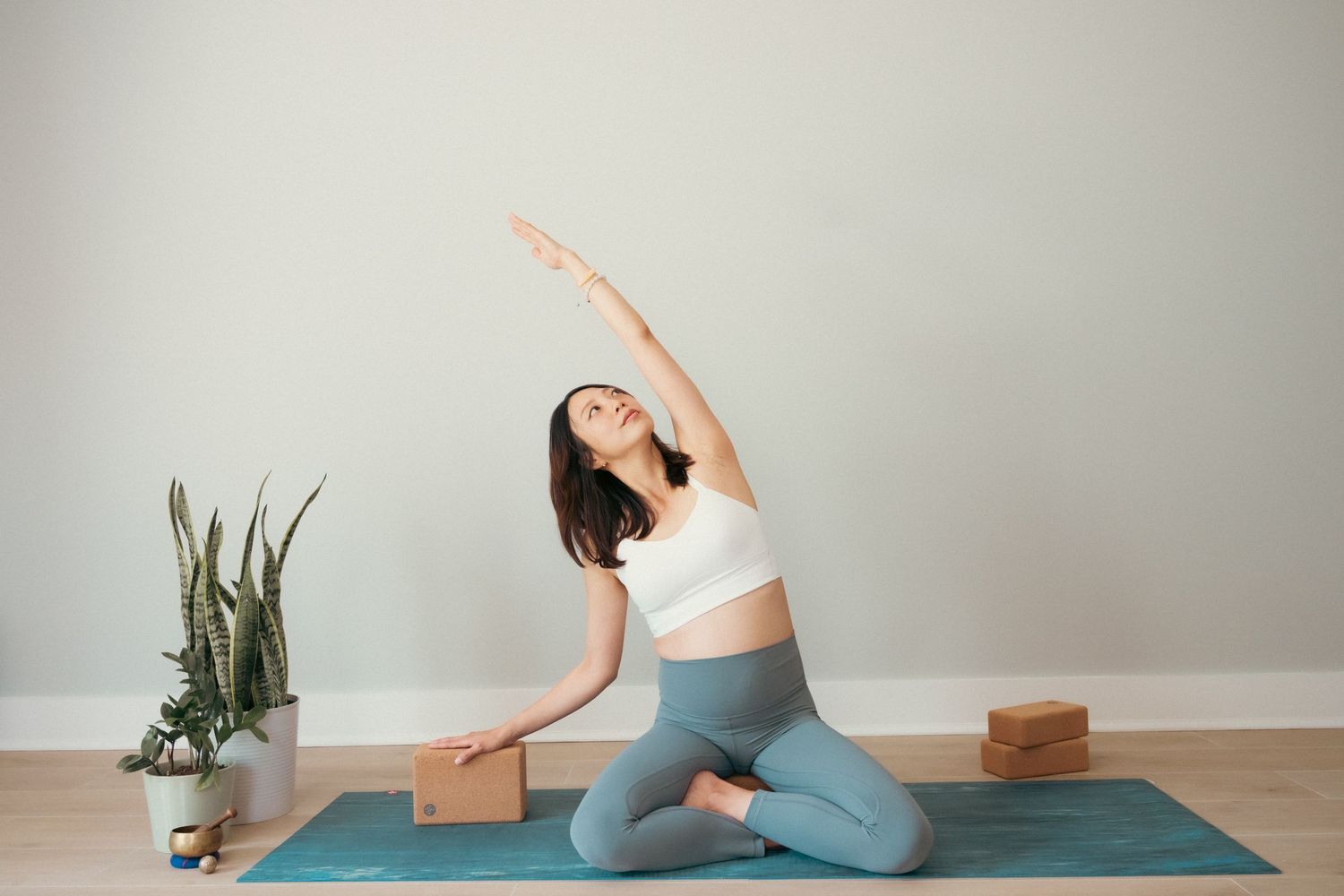 Yoga practitioner demonstrating stretching poses on a blue mat with props in a bright room.