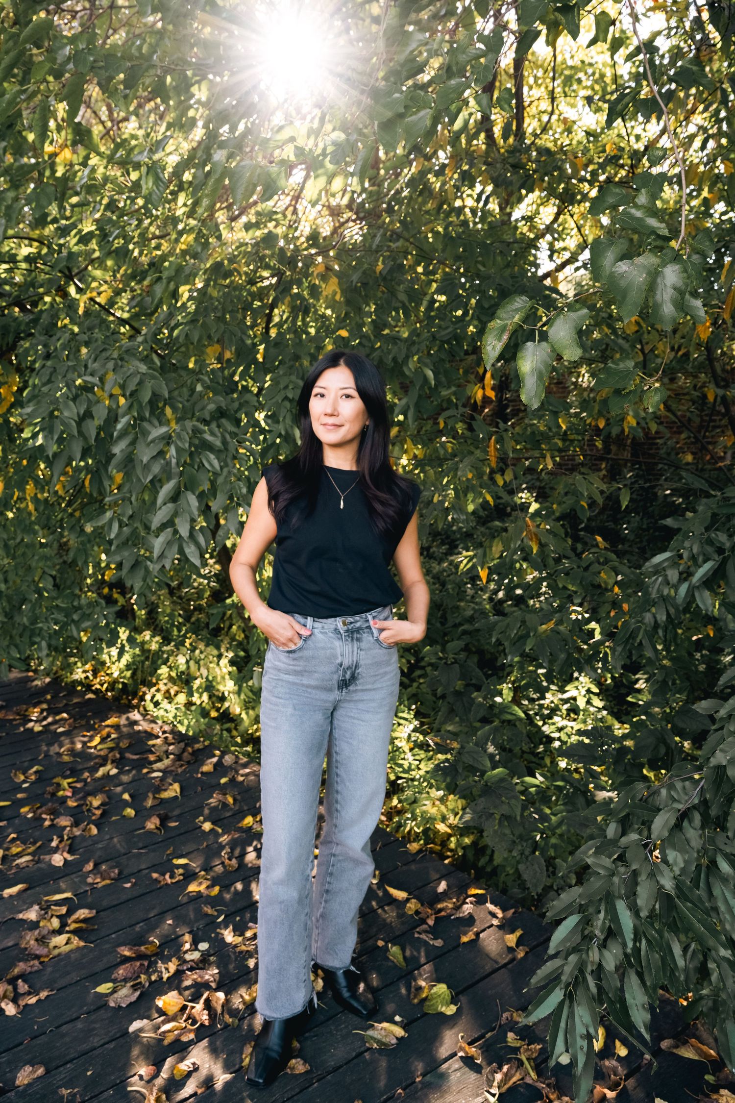 Sunlit garden photoshoot with denim and black casual wear among green foliage.