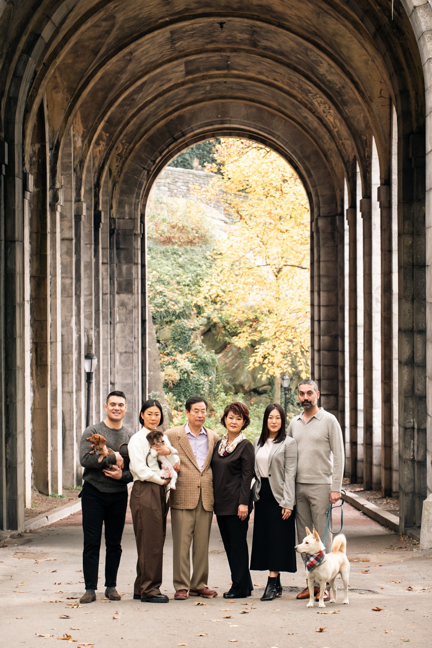 A group stands together in a dramatic stone archway tunnel with autumn foliage visible.