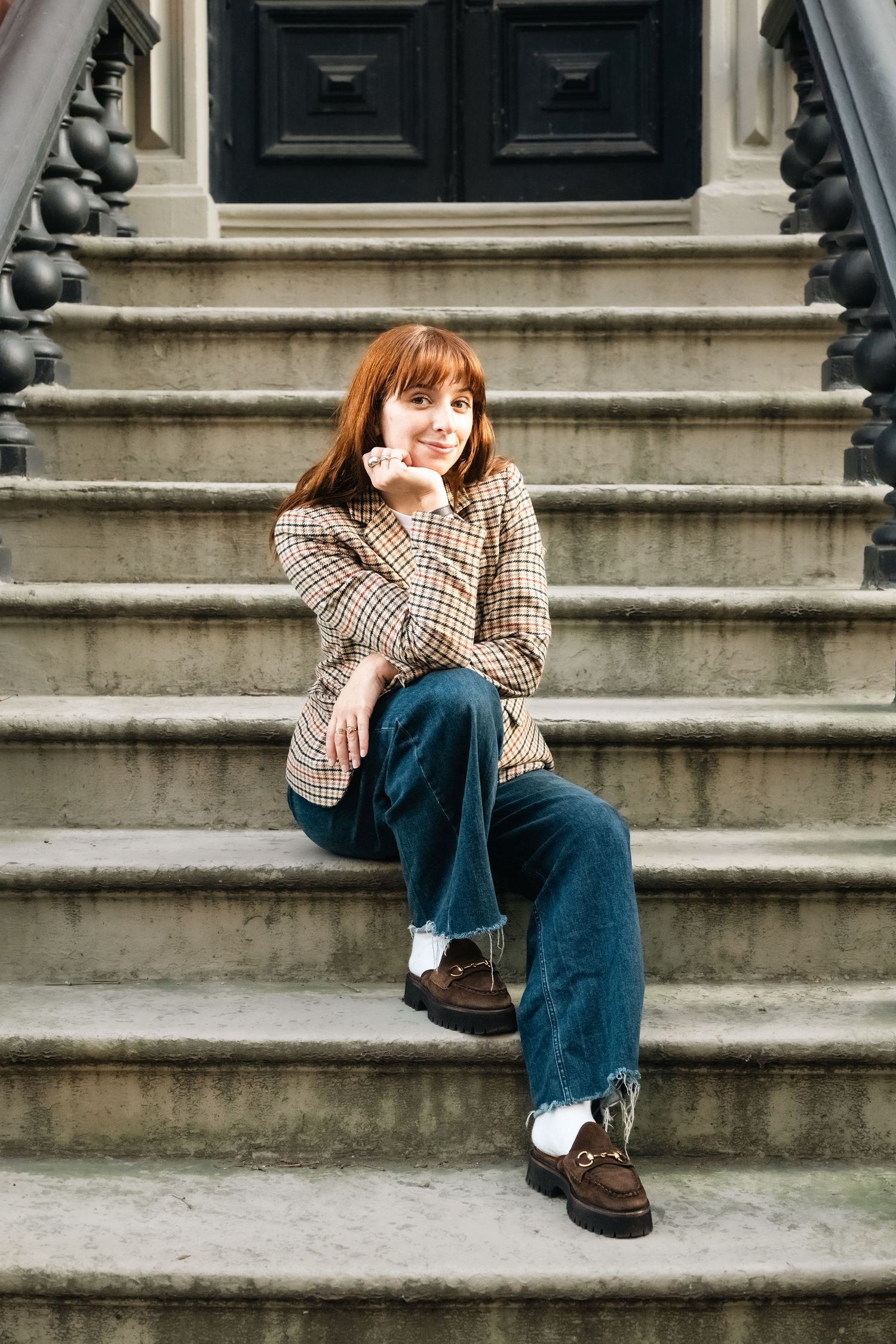 Person in plaid shirt and jeans sitting on concrete steps outdoors.