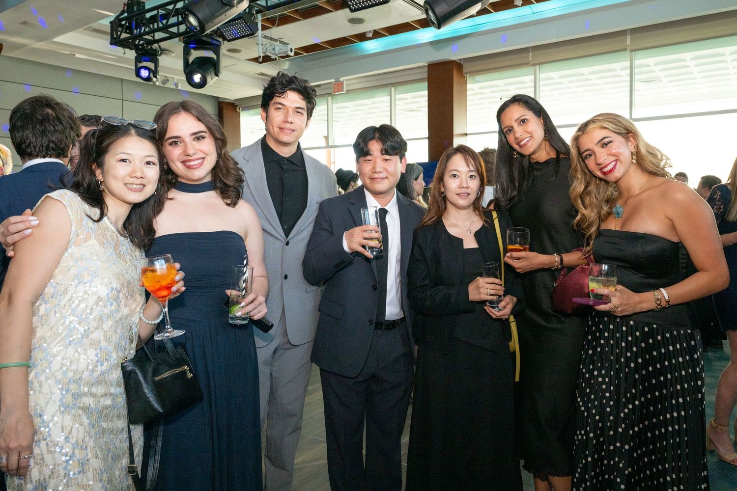 Group of seven elegantly dressed guests smiling and holding drinks at a formal evening gala event.
