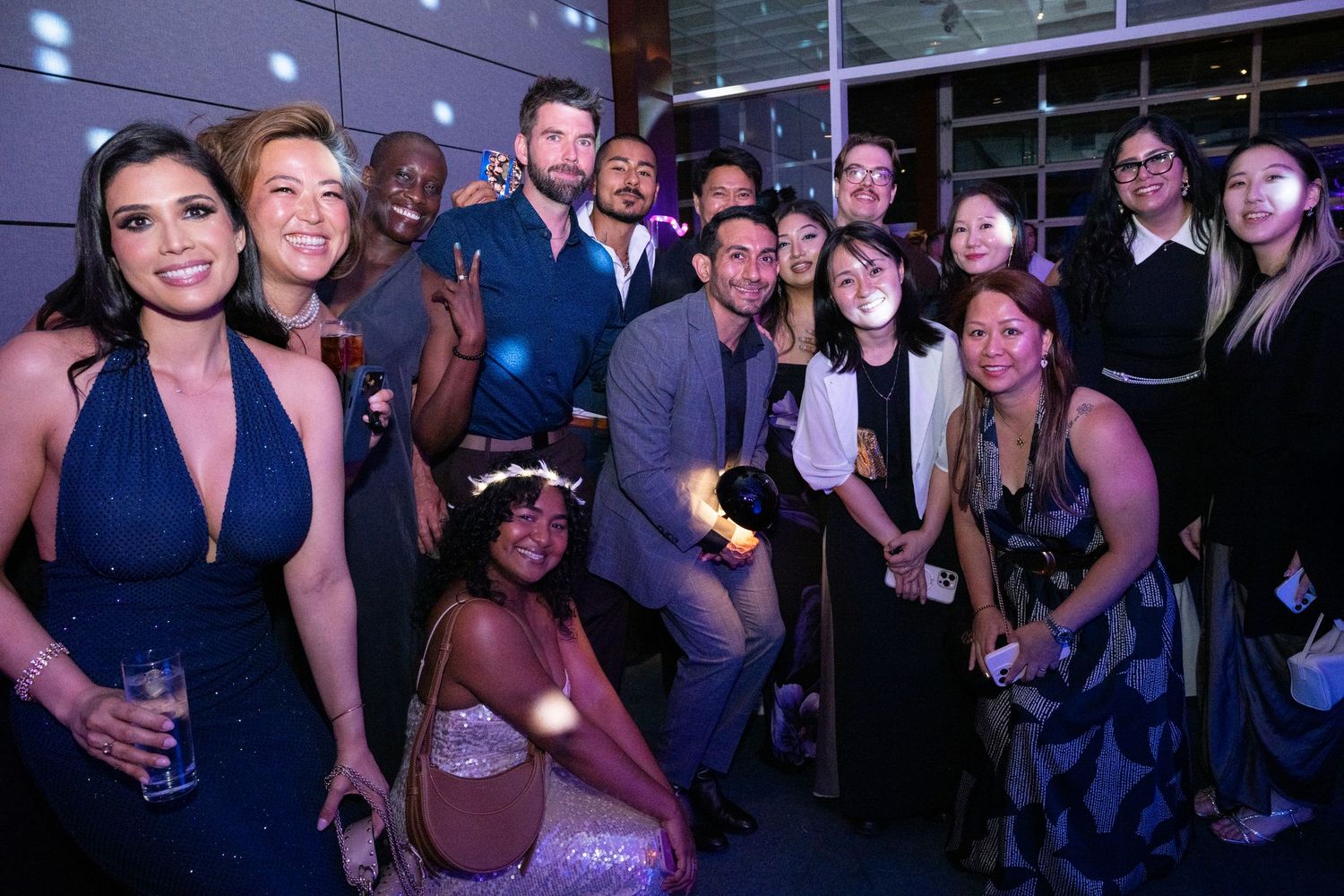 A large group of elegantly dressed guests pose together smiling at a formal evening gala event.